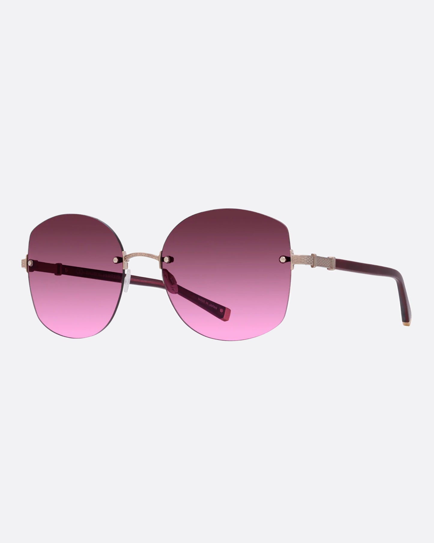 A pair of rose gold titanium frame sunglasses with pink cat eye lenses. Shown from the side.