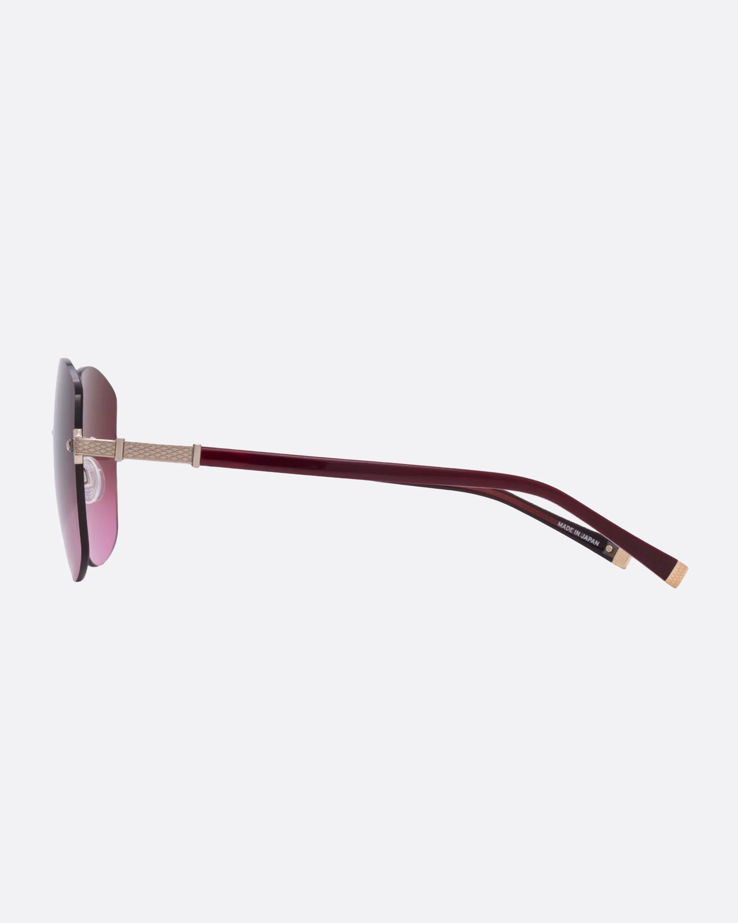 A pair of rose gold titanium frame sunglasses with pink cat eye lenses. Shown from the side.