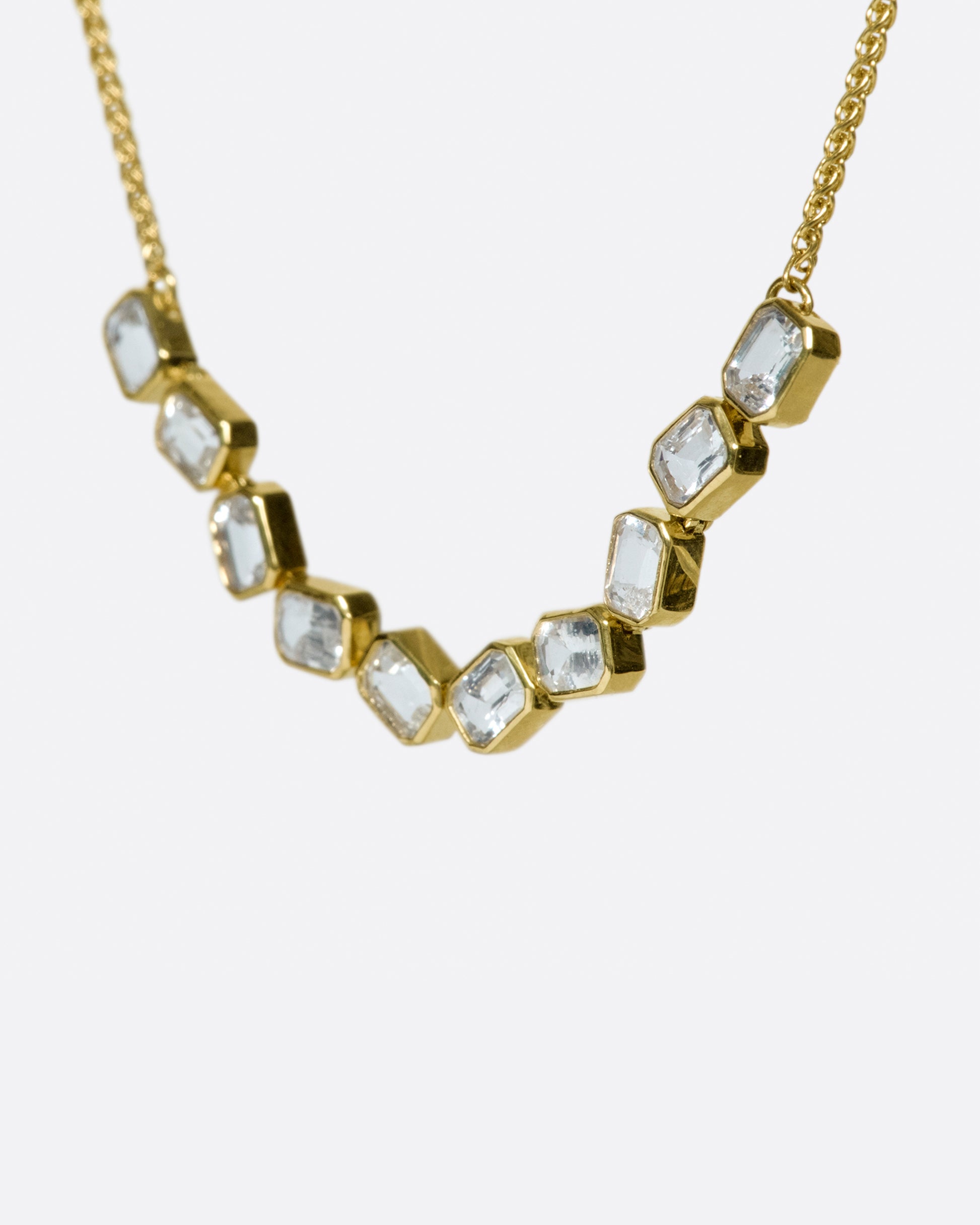 A chain necklace with a section of ten bezel set, emerald cut, white sapphires each connected to its neighbor by a hinge so the whole piece moves fluidly.