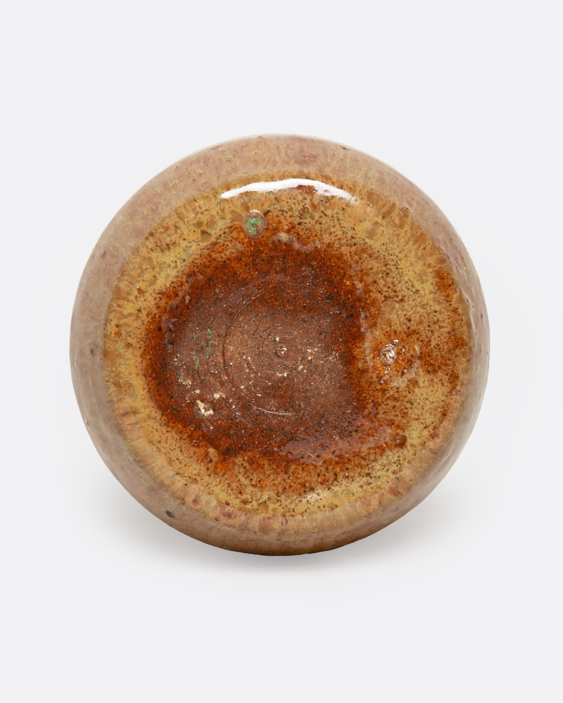 A tan ceramic vase with a dripped umber glaze, shown from the bottom.