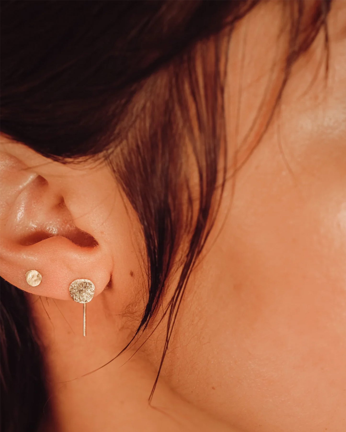 A yellow gold hammered dot stud earring, shown on an ear.