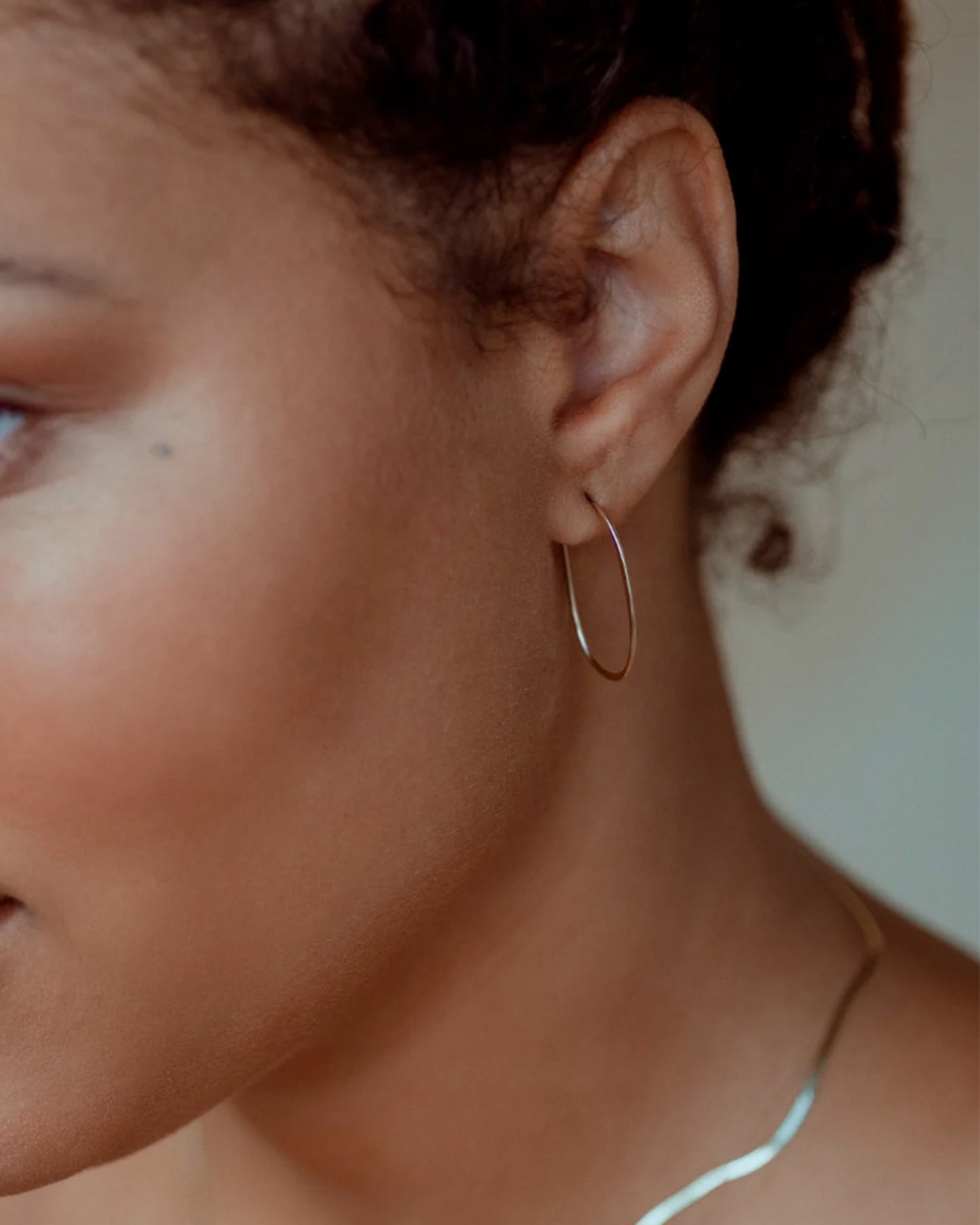 A pair of yellow gold, oval, hammered wire hoops with a hook closure, shown on an ear.