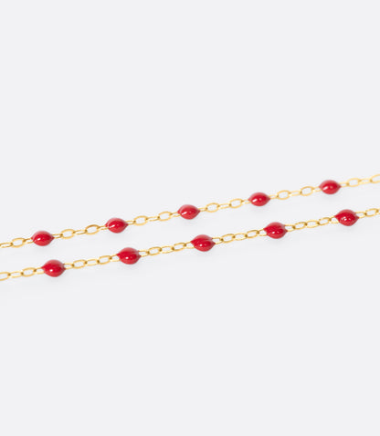A close up view of a yellow gold cable chain bracelet with red resin droplets. 