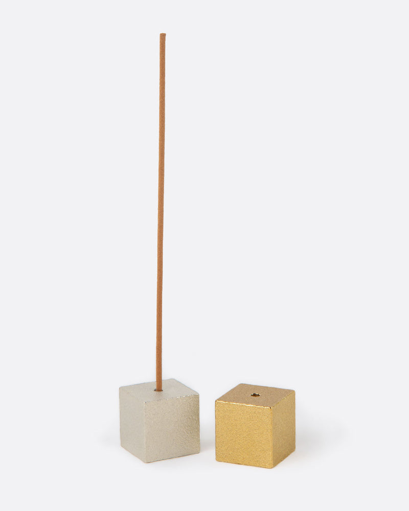 Large brass cube incense holder, a small solid brass cube holding an incense stick, beside a white cube