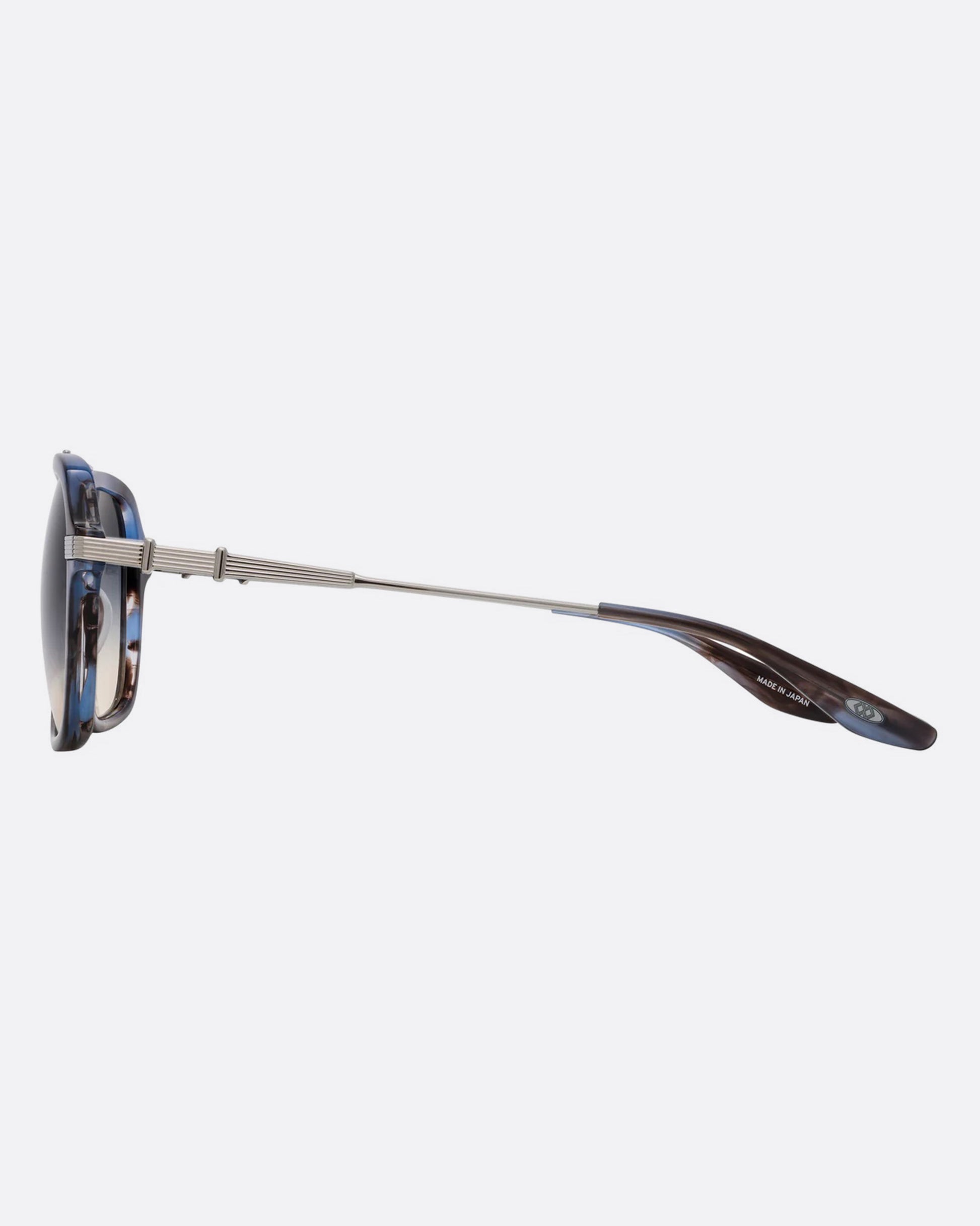 A pair of navigator sunglasses  with pearly blue and silver structured frames and gray gradient lenses. Shown from the side.