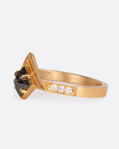 A yellow gold ring with a central black diamond with white diamond details on both sides of the band. Shown from the sid.
