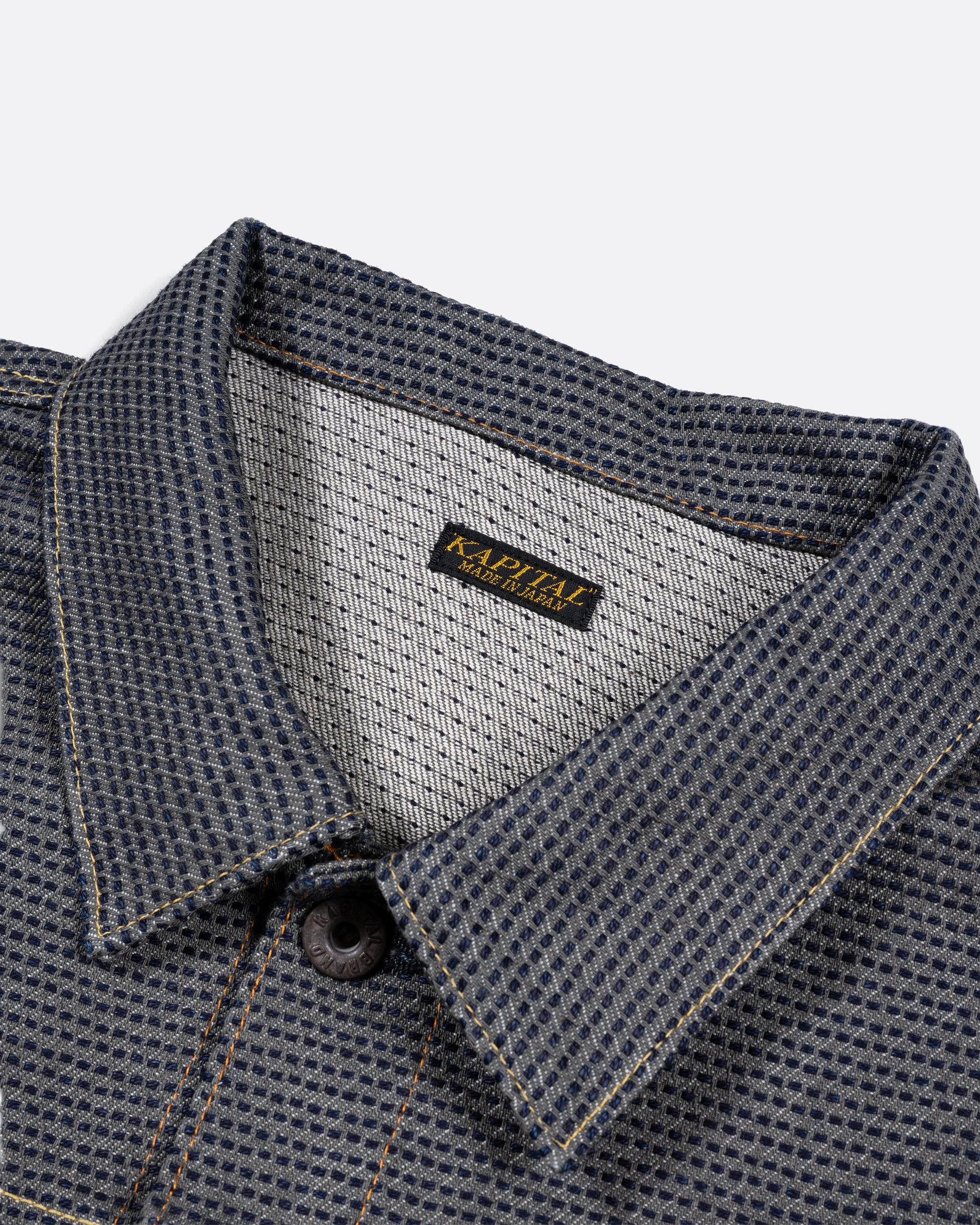 A dark blue textured button down denim jacket with a single pocket. Close up of the collar.