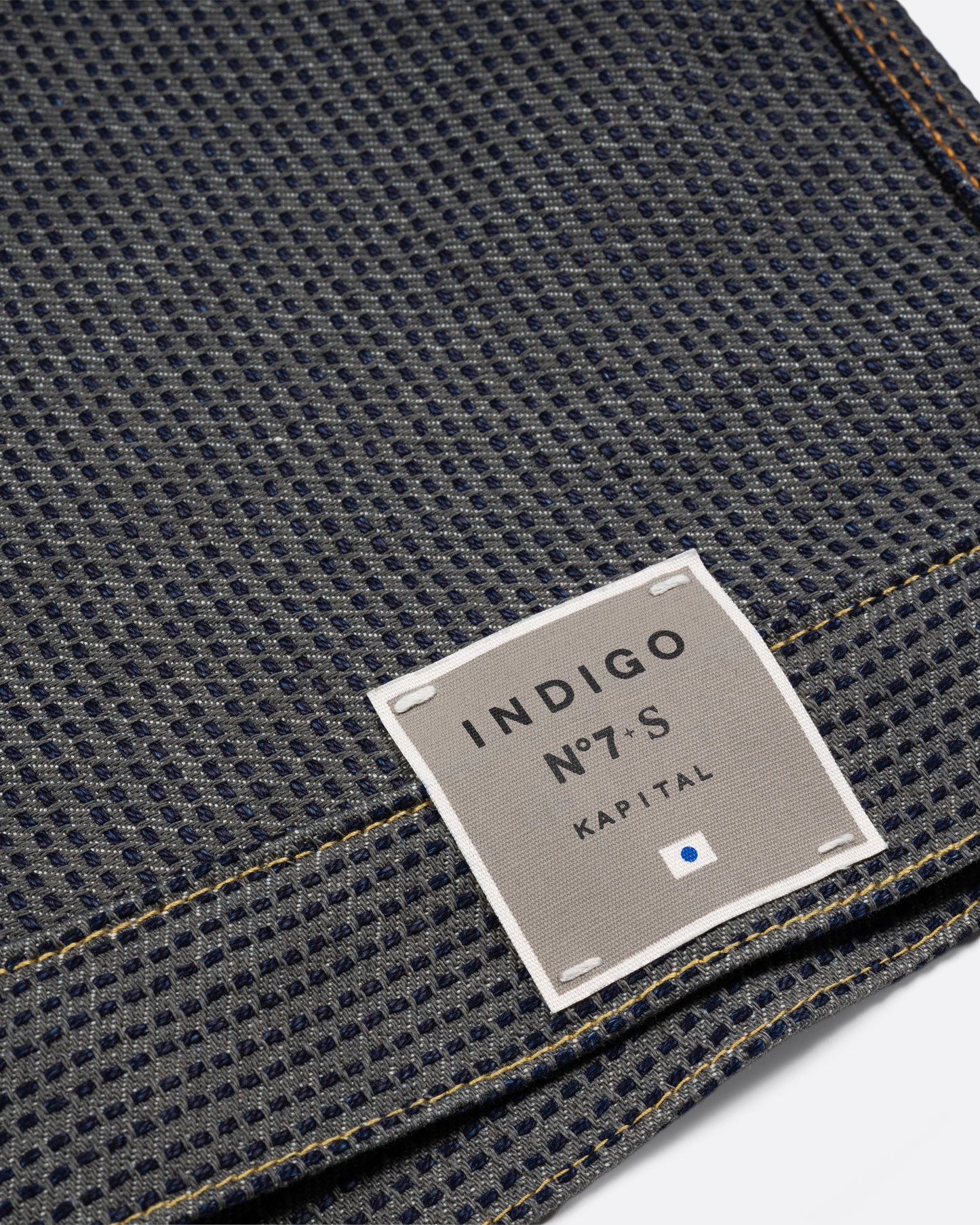 A dark blue textured button down denim jacket with a single pocket. Close up of the label on the hem.