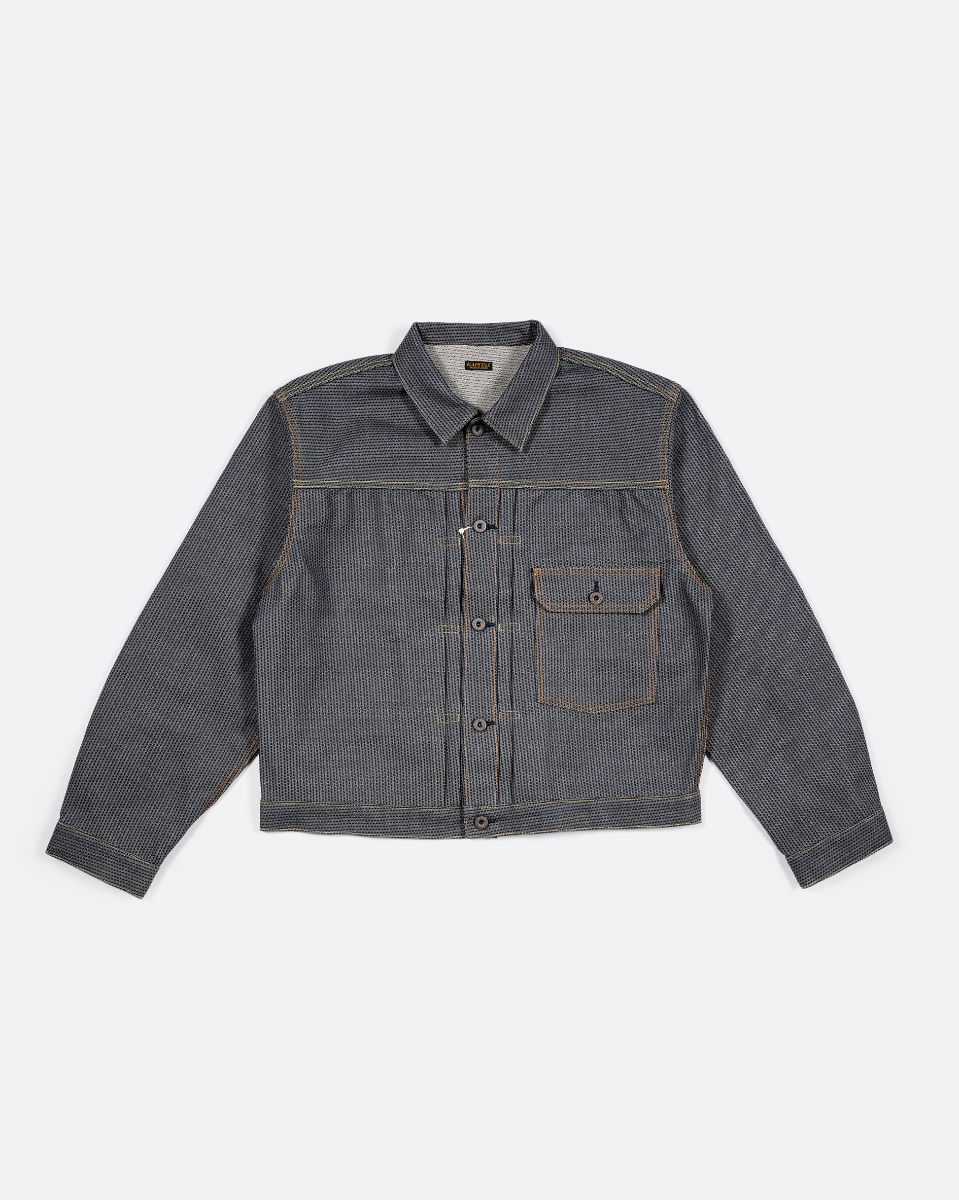 A dark blue textured button down denim jacket with a single pocket. View laying flat.