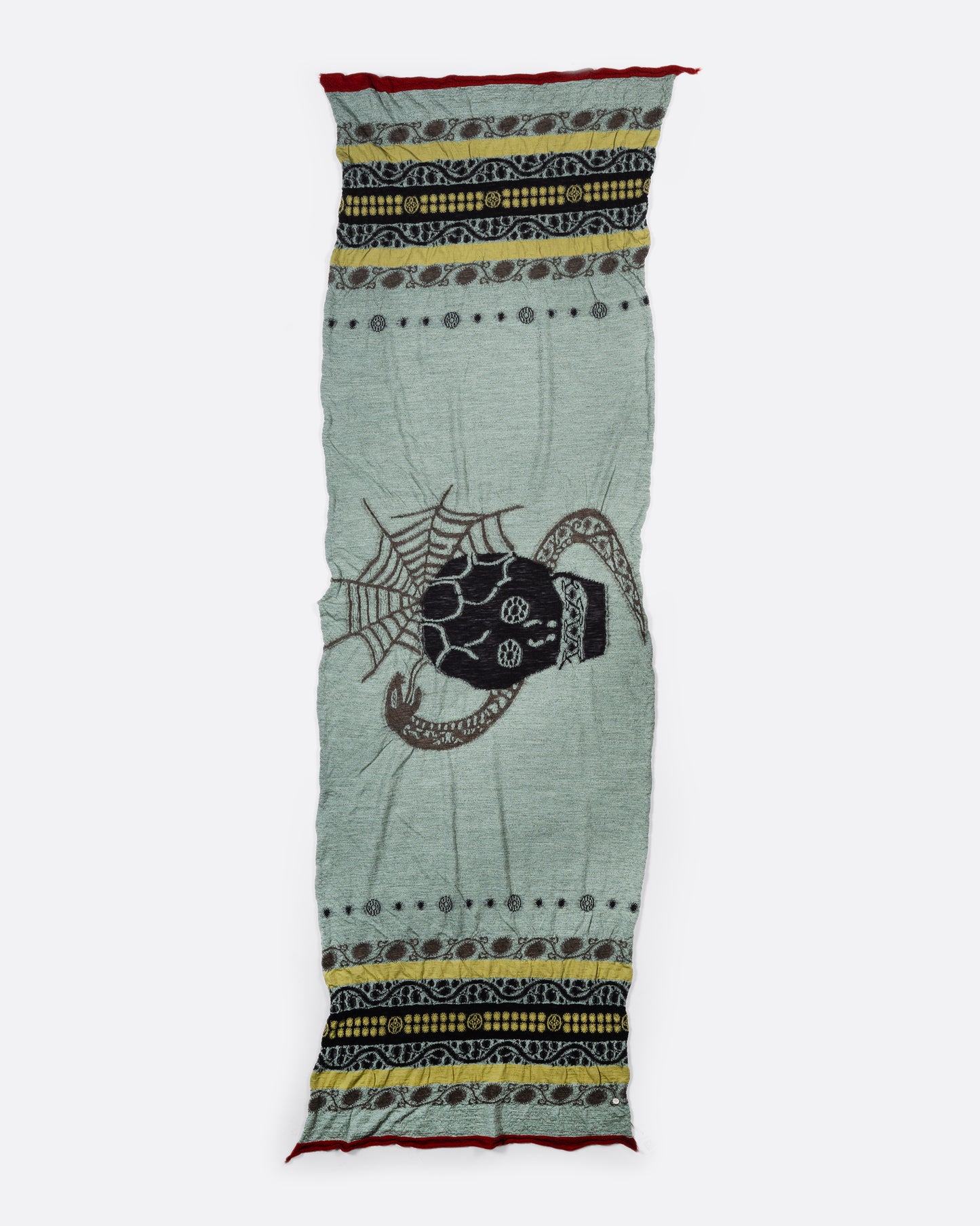A grey and green wool scarf with a black skull in the center. View laid flat.