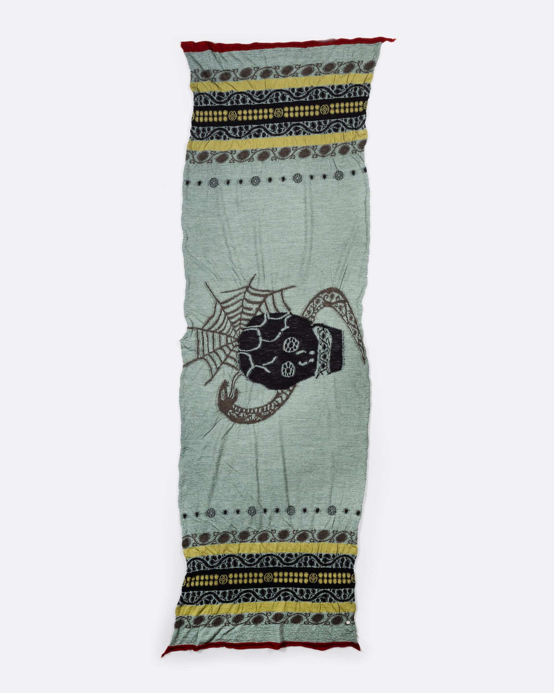 A grey and green wool scarf with a black skull in the center. View laid flat.