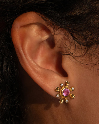 Audrius Krulis flower stud earring in yellow gold worn on an ear, a round pink sapphire center with gold petals tipped in diamonds