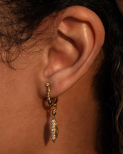 Audrius Krulis leaf drop earring in yellow gold worn on an ear, a textured leaf set with a line of diamonds hanging from a beaded hoop