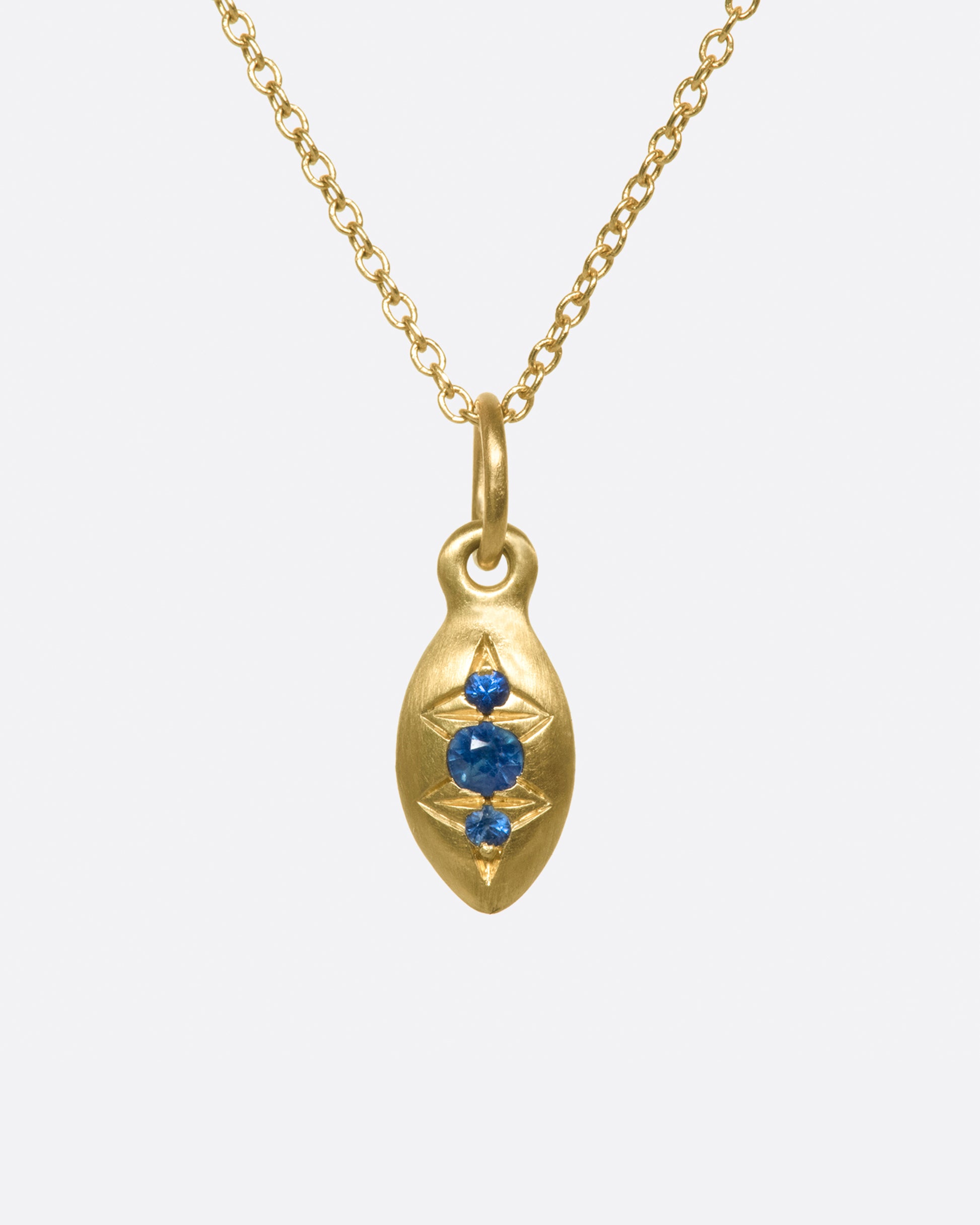 A seed-shaped, brushed gold pendant necklace with three vibrant blue sapphires.