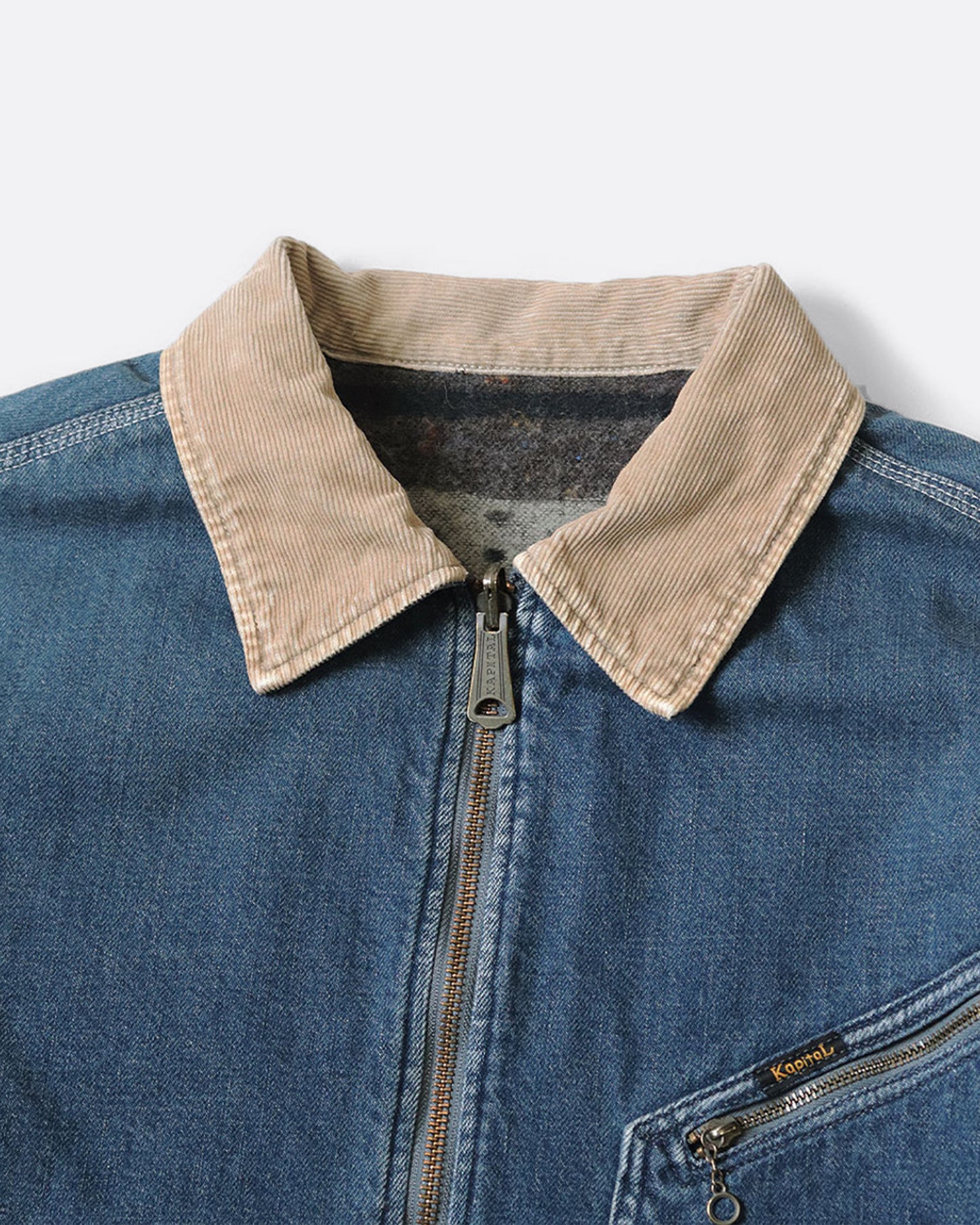 A close up of a blue denim work jacket with a beige collar, lined in wool with a skeleton print. 