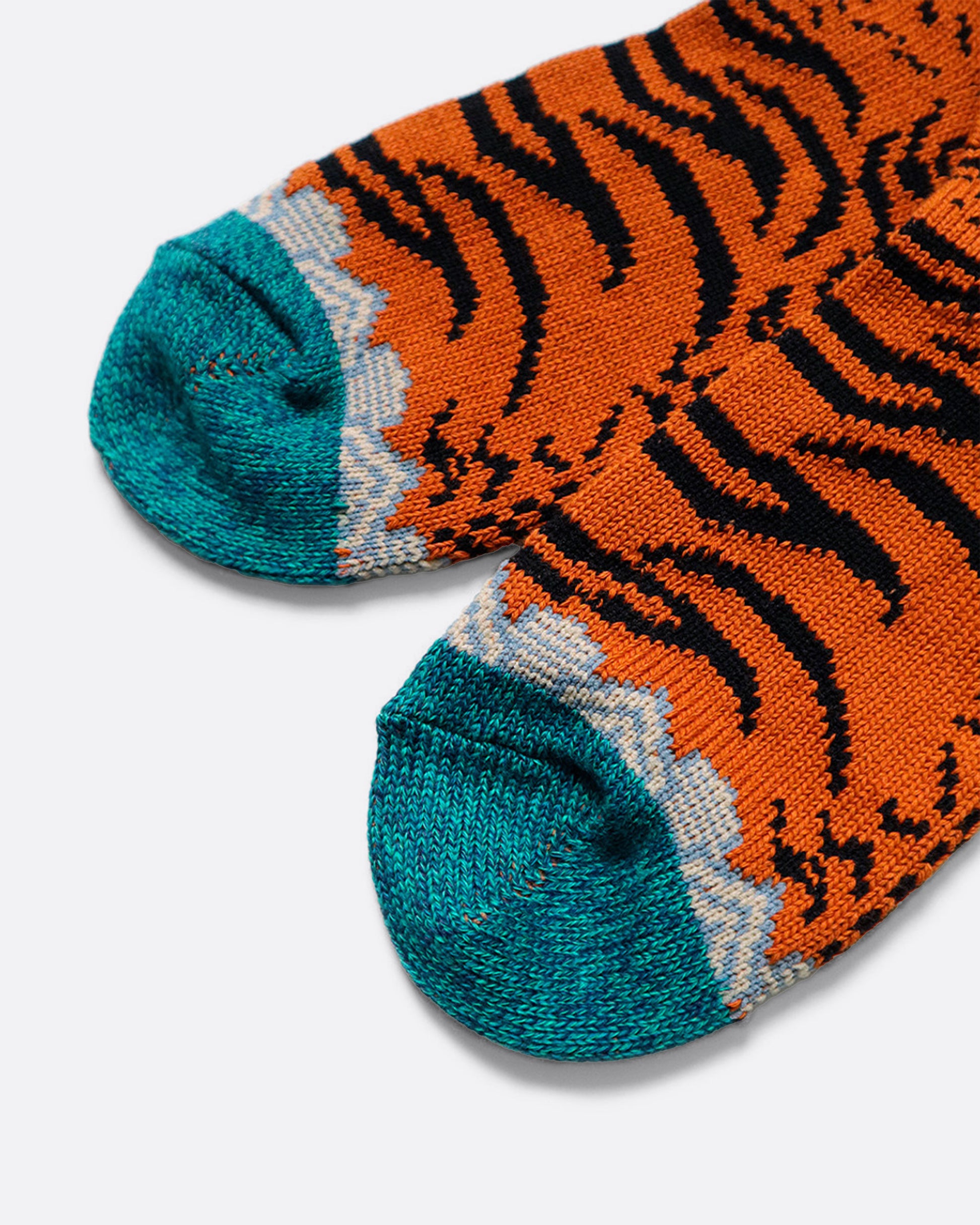 A close up of the toes of a pair of orange, teal, and black Nepalese tiger printed socks. Shown from the side.