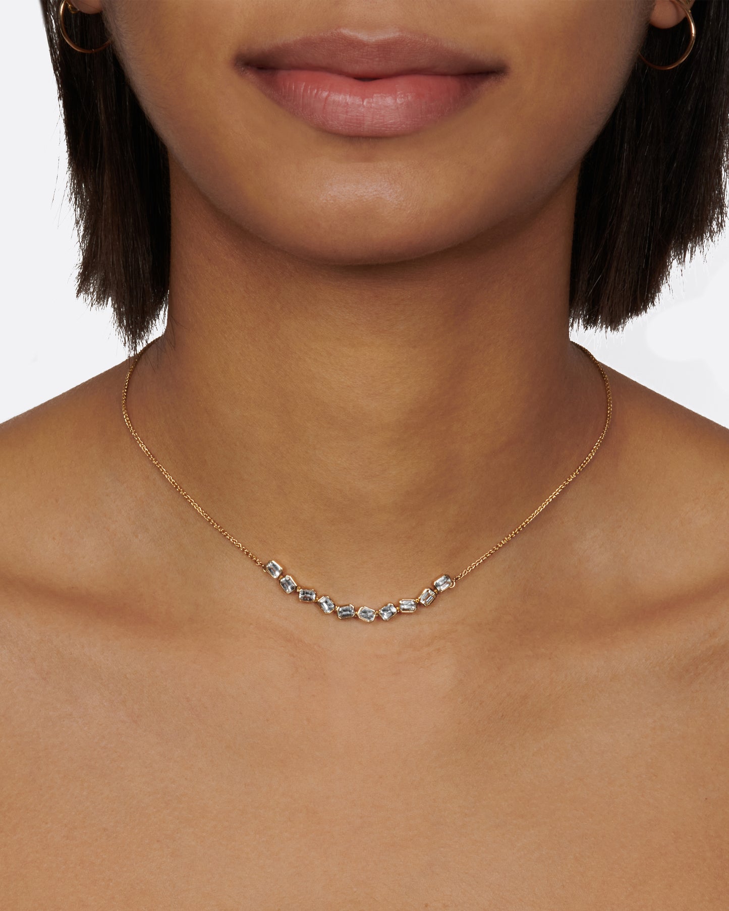 A chain necklace with a section of ten bezel set, emerald cut, white sapphires each connected to its neighbor by a hinge so the whole piece moves fluidly.