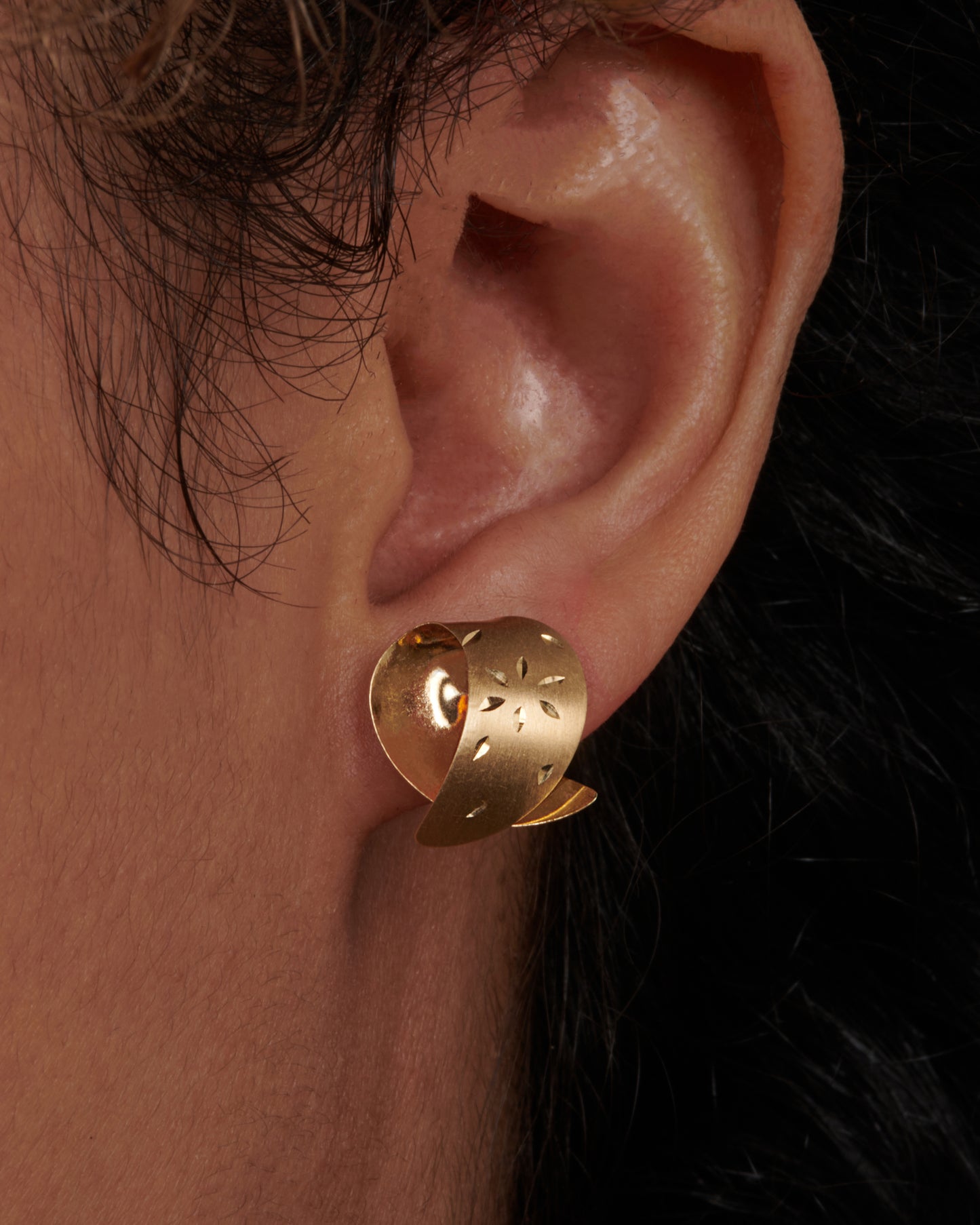 These vintage lightweight, folded studs are made of both matte and polished 14K gold. They're engraved with floral details that pick up light as you move. View on an ear.