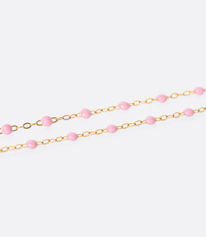 A close up view of a yellow gold cable chain bracelet with pink resin droplets. 