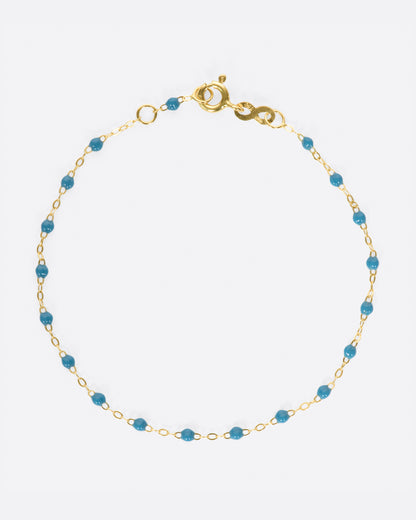 A yellow gold cable chain bracelet with droplets of blue resin. Shown closed from the top.