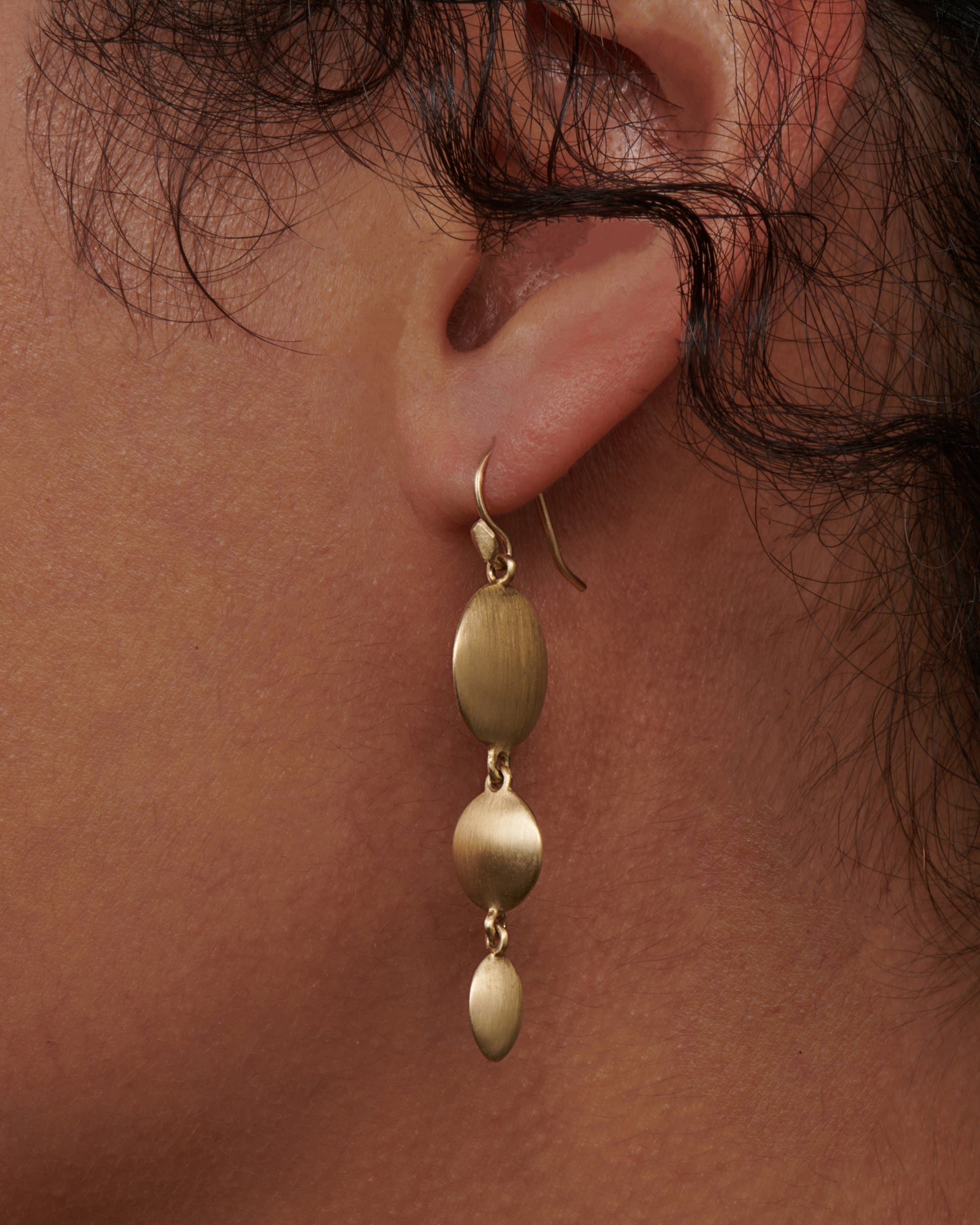 These unusual triple drop brushed gold earrings have impressive razor thin edges that make them look different from every angle. View on an ear.