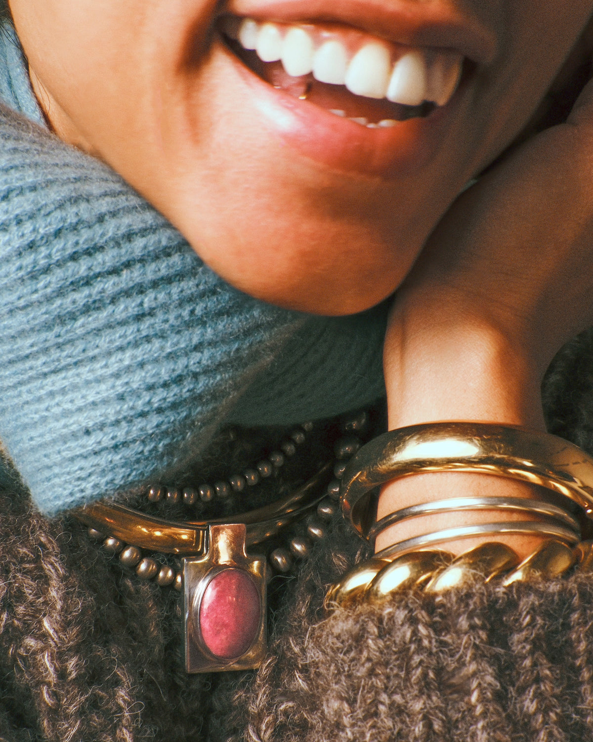 A wide yellow gold oval hinged bangle shown styled with gold and silver bracelets and necklaces.
