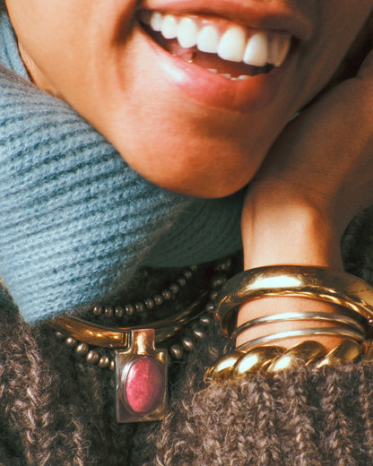 Vintage yellow gold cuff bracelet, a model in a blue knit scarf wearing the cuff stacked with other gold bangles, with a gemstone pendant necklace