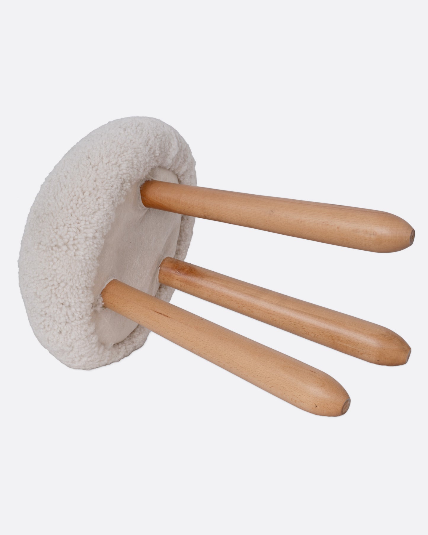 A domed shearling stool with three wooden legs, shown from the side lying down.