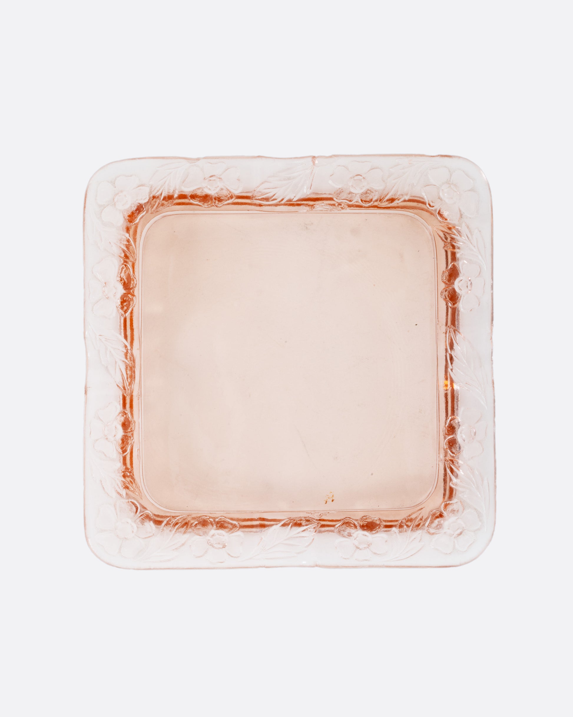A square pink glass ashtray with a floral design on the edges, shown from the top.