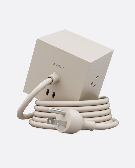 A tan cube shaped power strip with multiple outlets and a coiled cable, shown from the back.