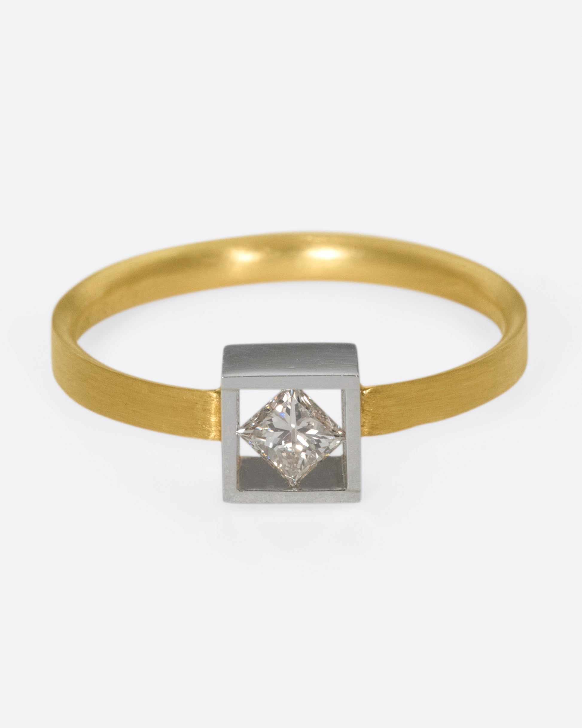 A geometric solitaire ring with a princess cut diamond set on its side in a platinum setting on a yellow gold band.