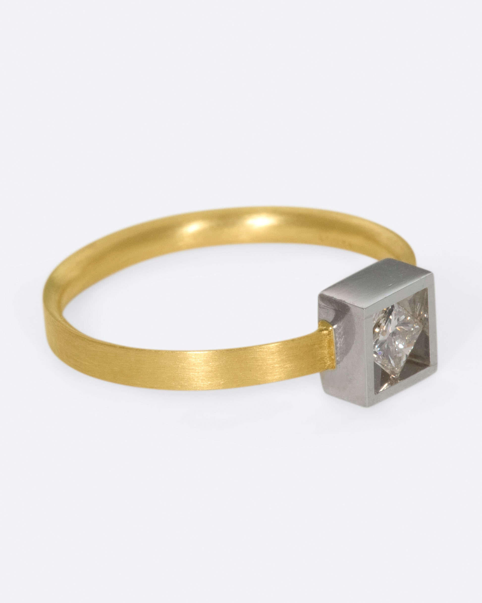 A geometric solitaire ring with a princess cut diamond set on its side in a platinum setting on a yellow gold band.