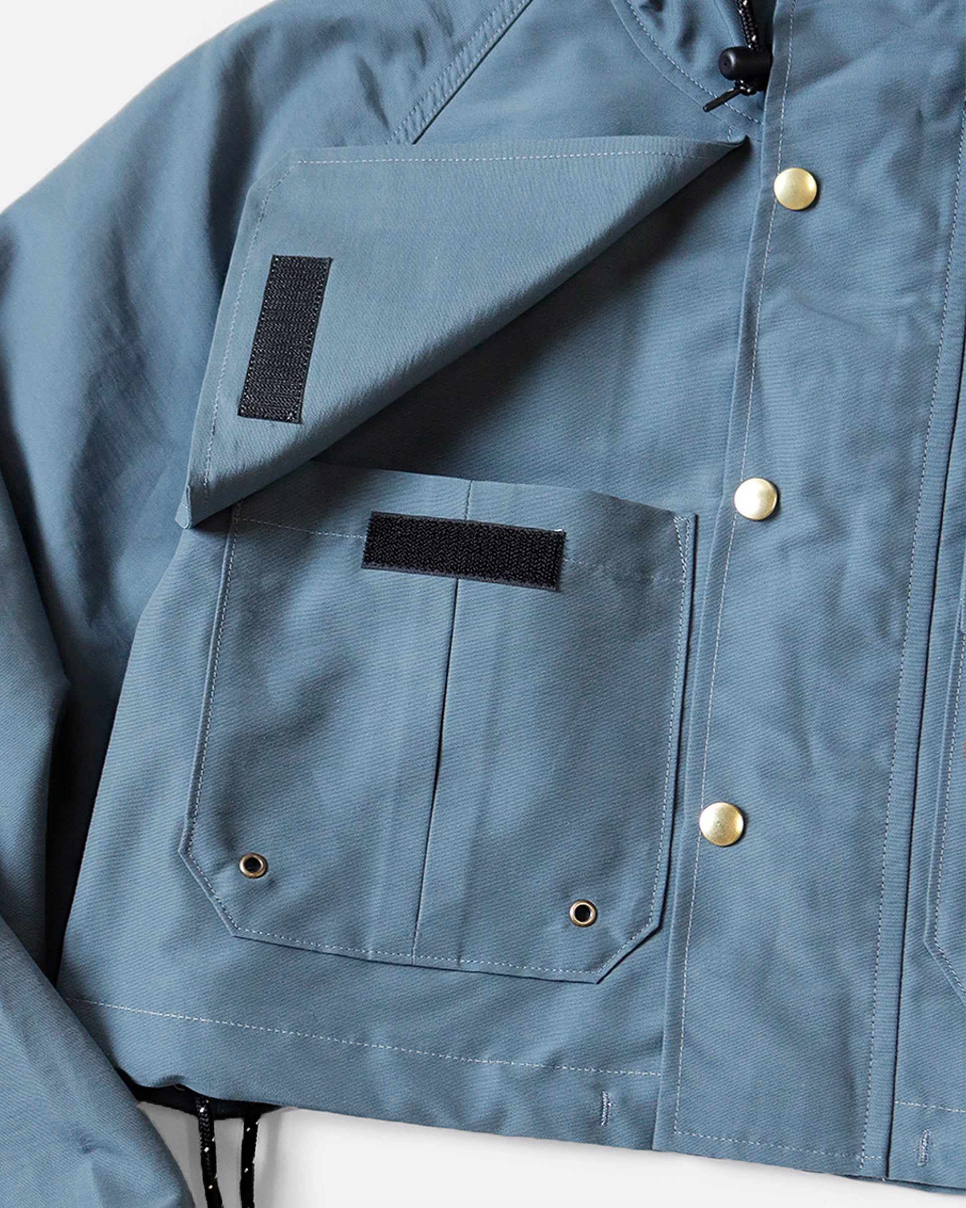 Cropped hooded rain jacket with two pockets in front. View from the front, close up of pocket.