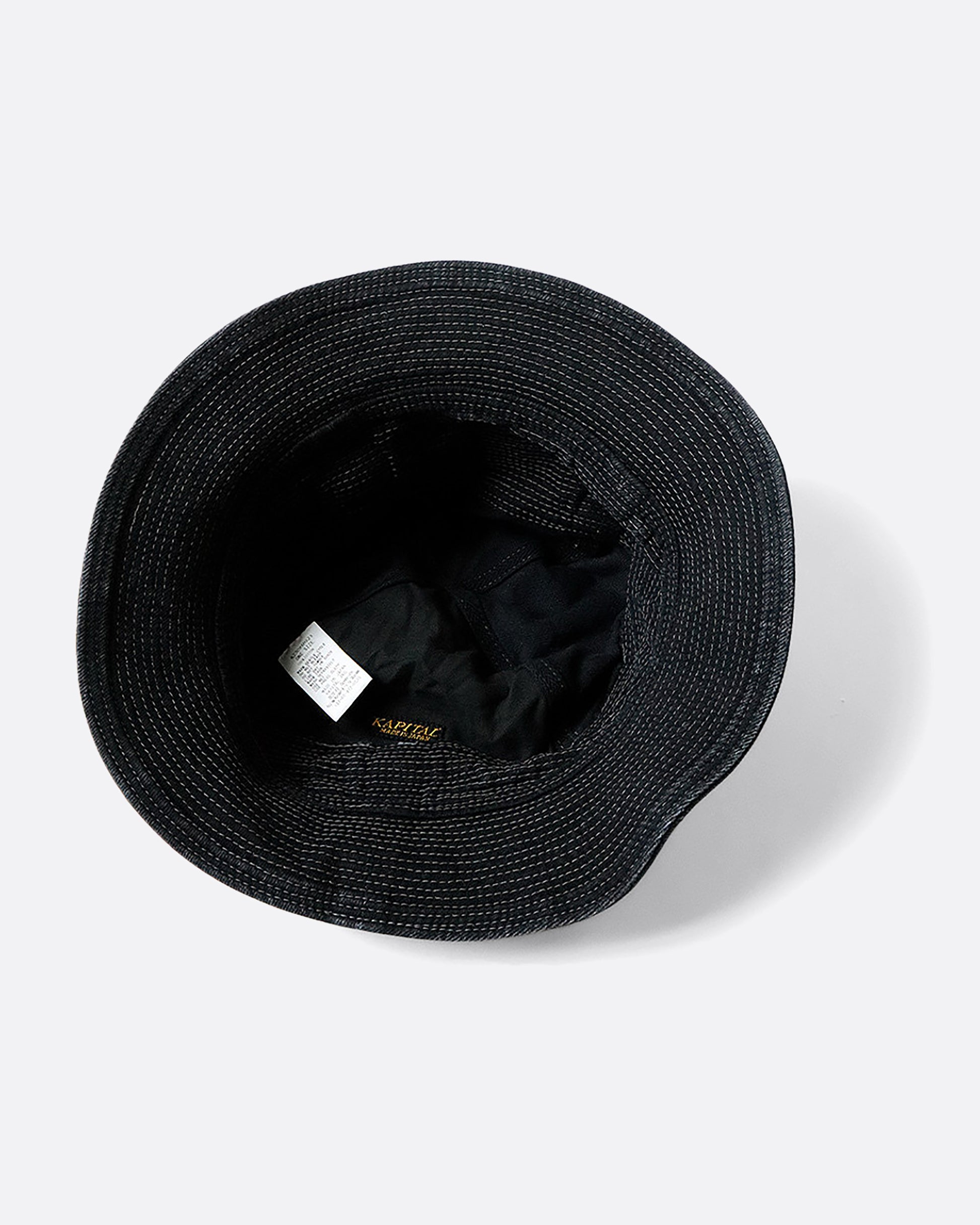 A black denim bucket hat with a buckle at the crown and contrast stitching throughout. View of the inside.