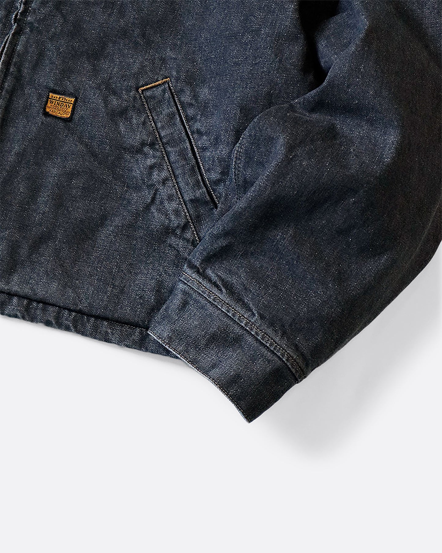 A dark blue denim bomber jacket with a corduroy collar and two front pockets. Close up of the cuff.