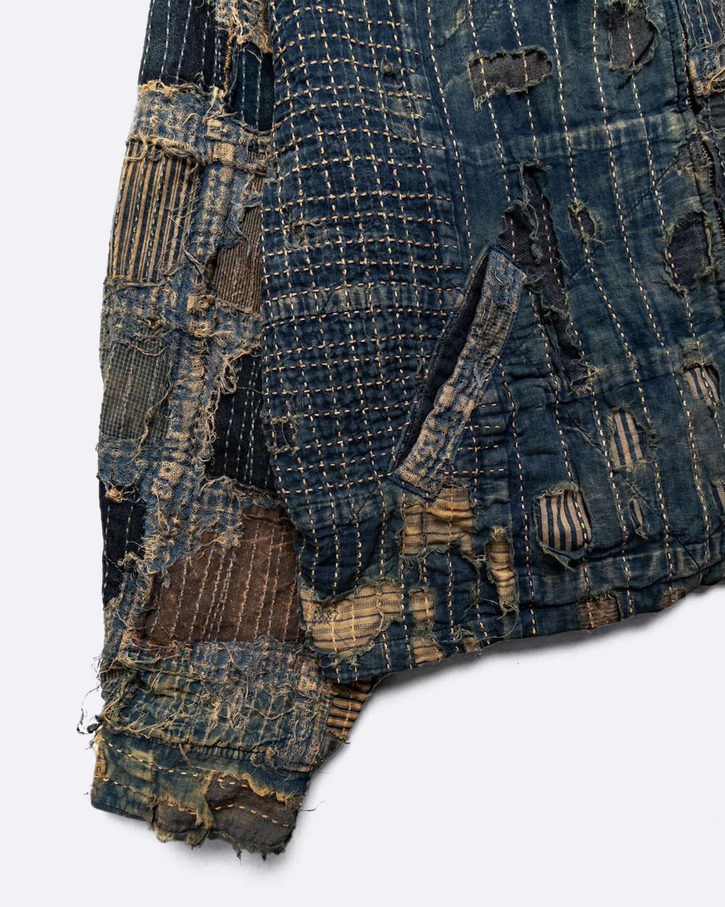 Distressed and repaired patchwork indigo jacket with pockets and front zipper. Close up view of pocket.