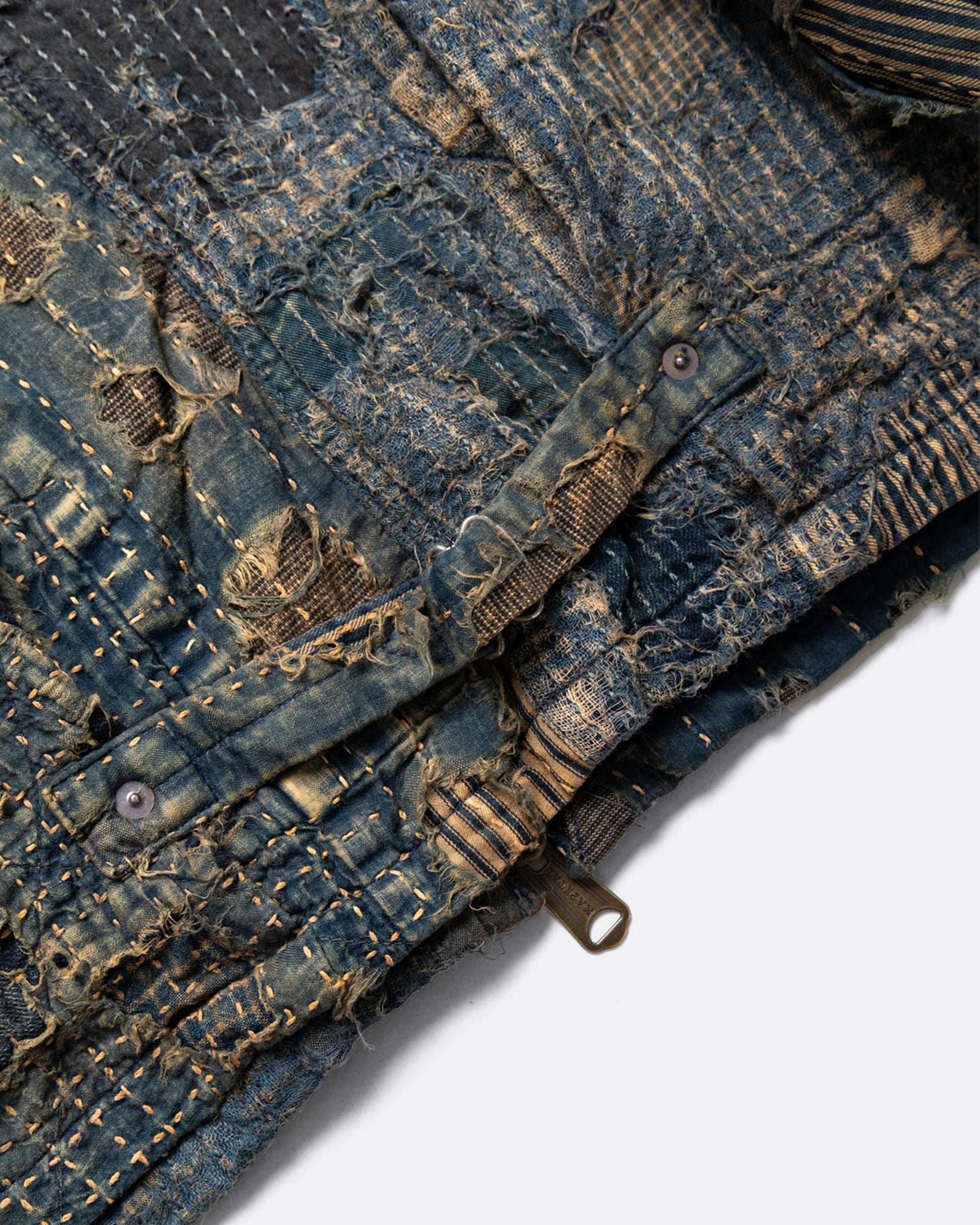 Distressed and repaired patchwork indigo jacket with pockets and front zipper. Close up view of adjustable lower back.