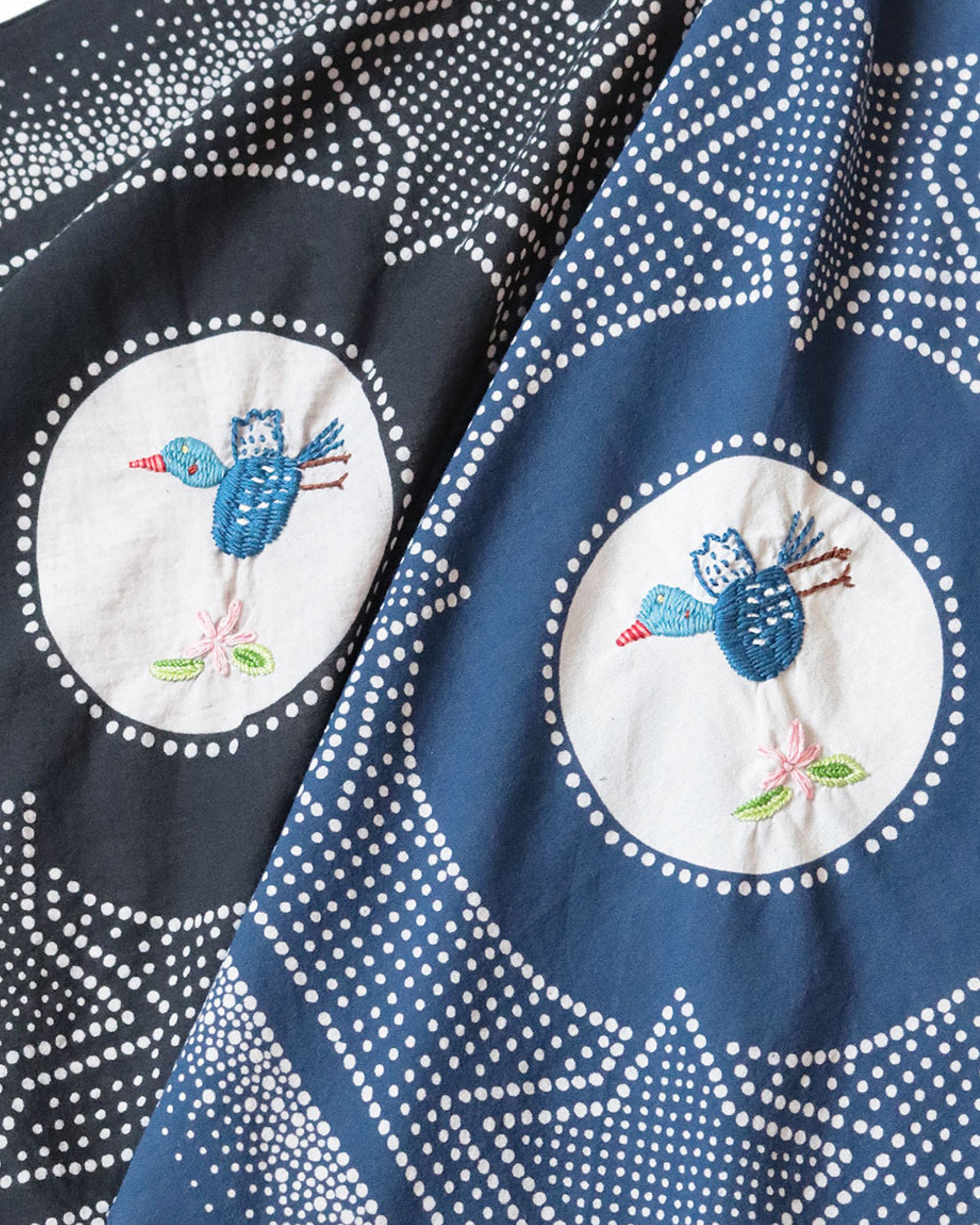 Two bandanas- one black and one navy with a white spotted star motif and a hand- embroidered magpie at the center. Shown close up from the front. 