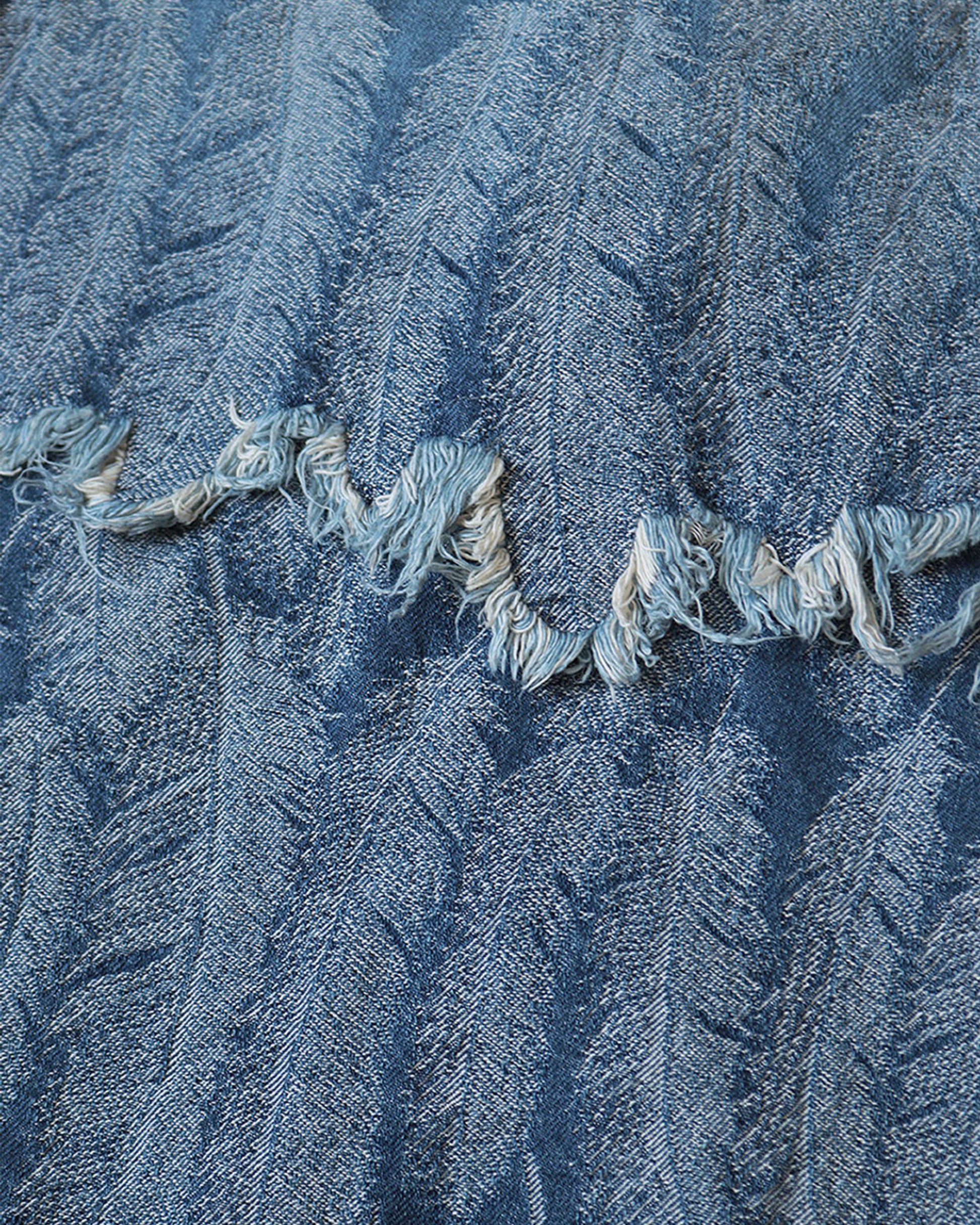 A close up of a raw edge seam on a light blue jacquard denim jacket with  an all- over feather motif.
