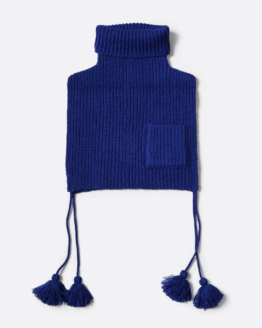 A blue loose knit bib poncho with a front pocket, long tassels, and a high neck, shown from the front. 