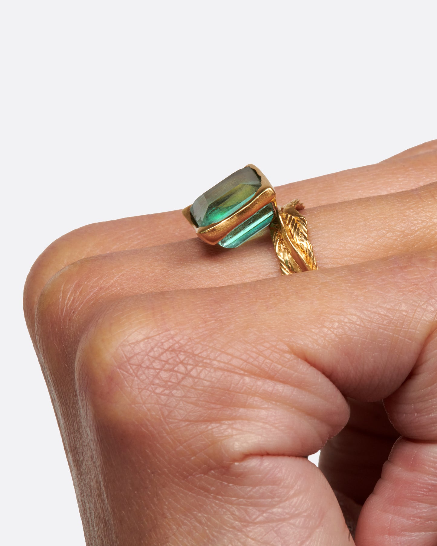 A gold braided band with a pale green square tourmaline.