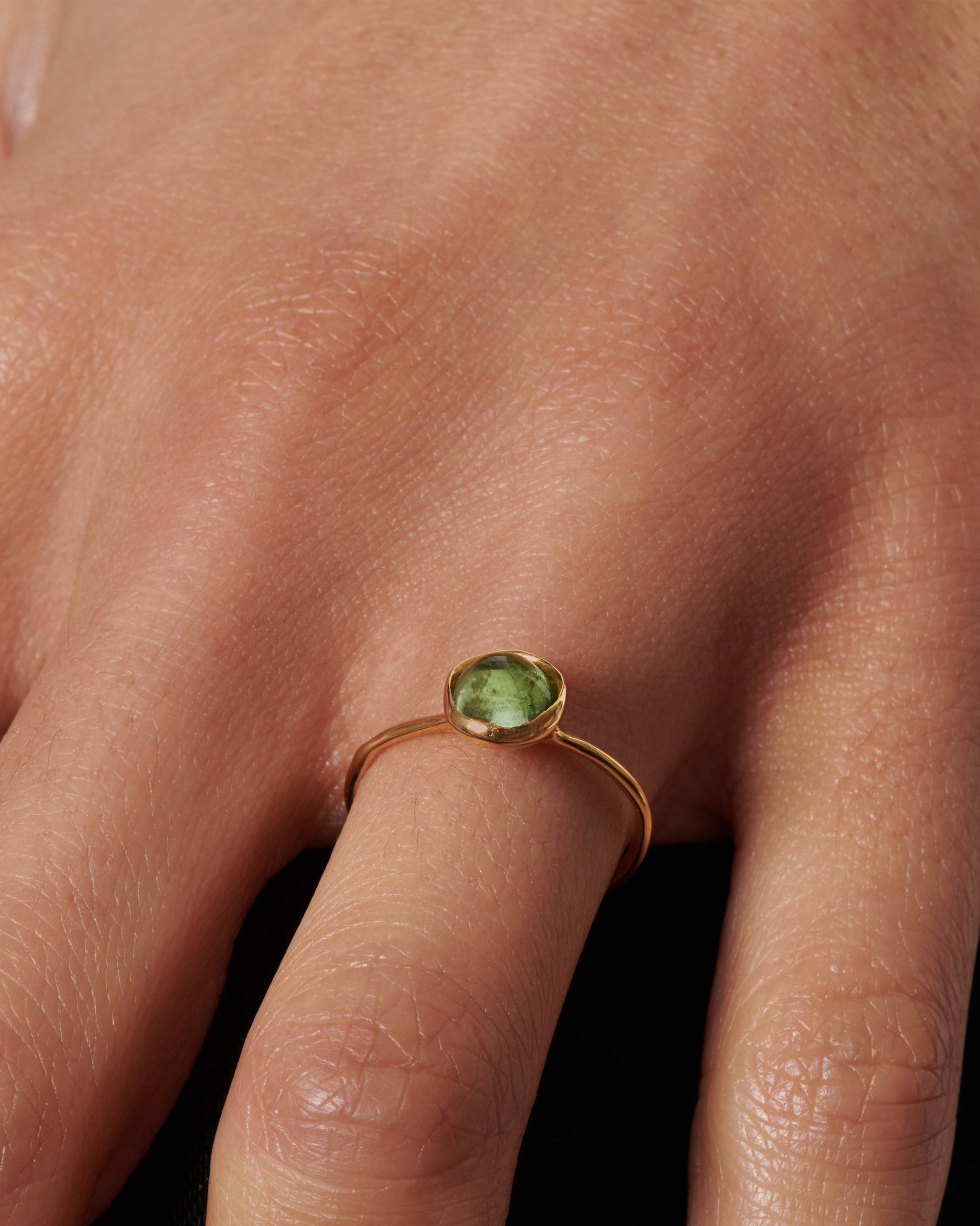 A sage-y green tourmaline cabochon is set in a bezel setting atop this ring.