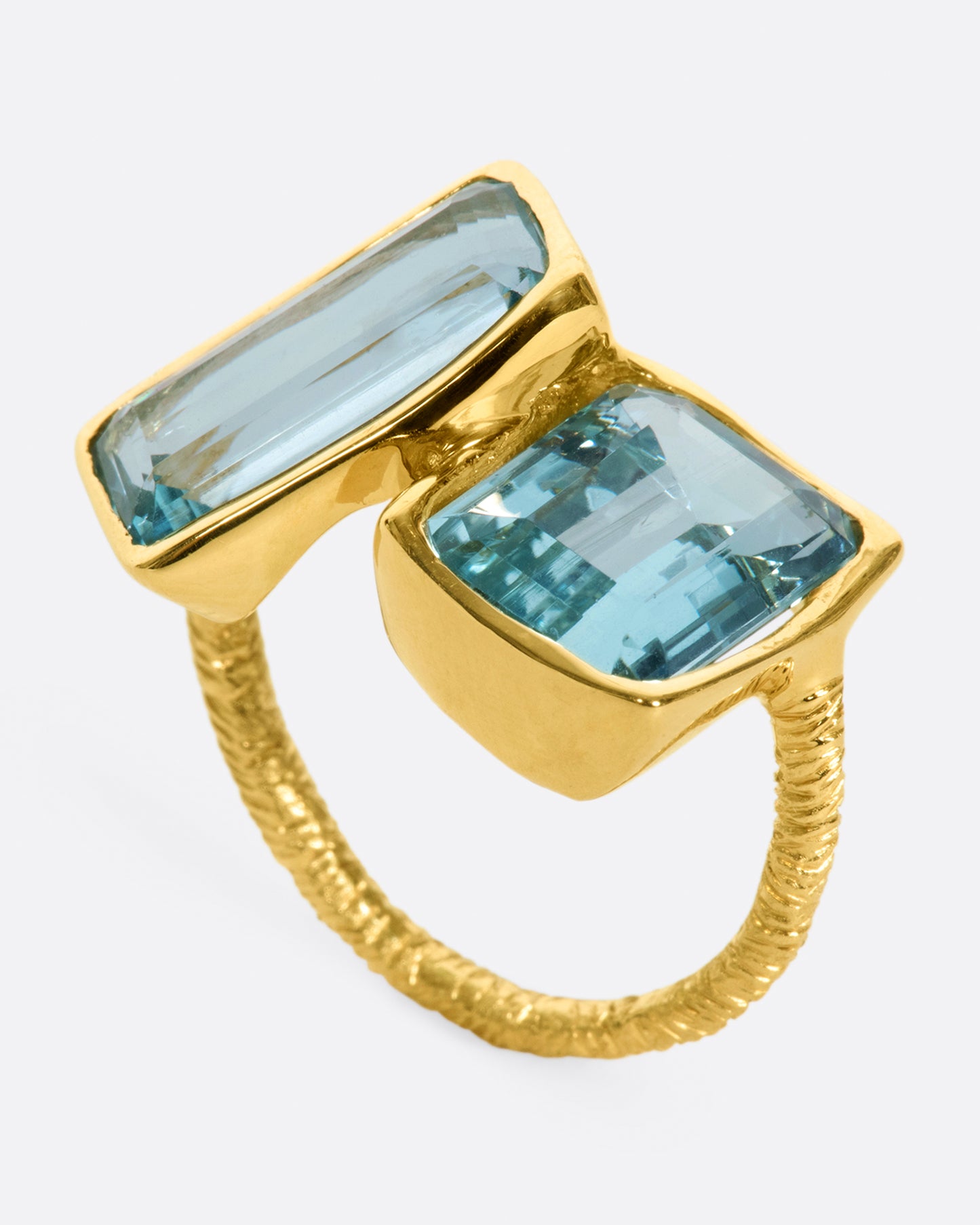 A yellow gold ring featuring two large emerald cut aquamarines set slightly askew