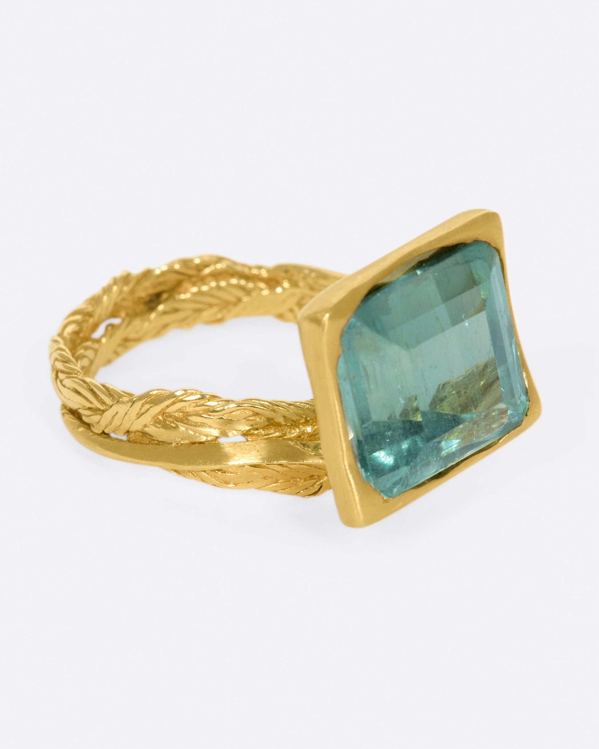 A gold braided band with a pale green square tourmaline.