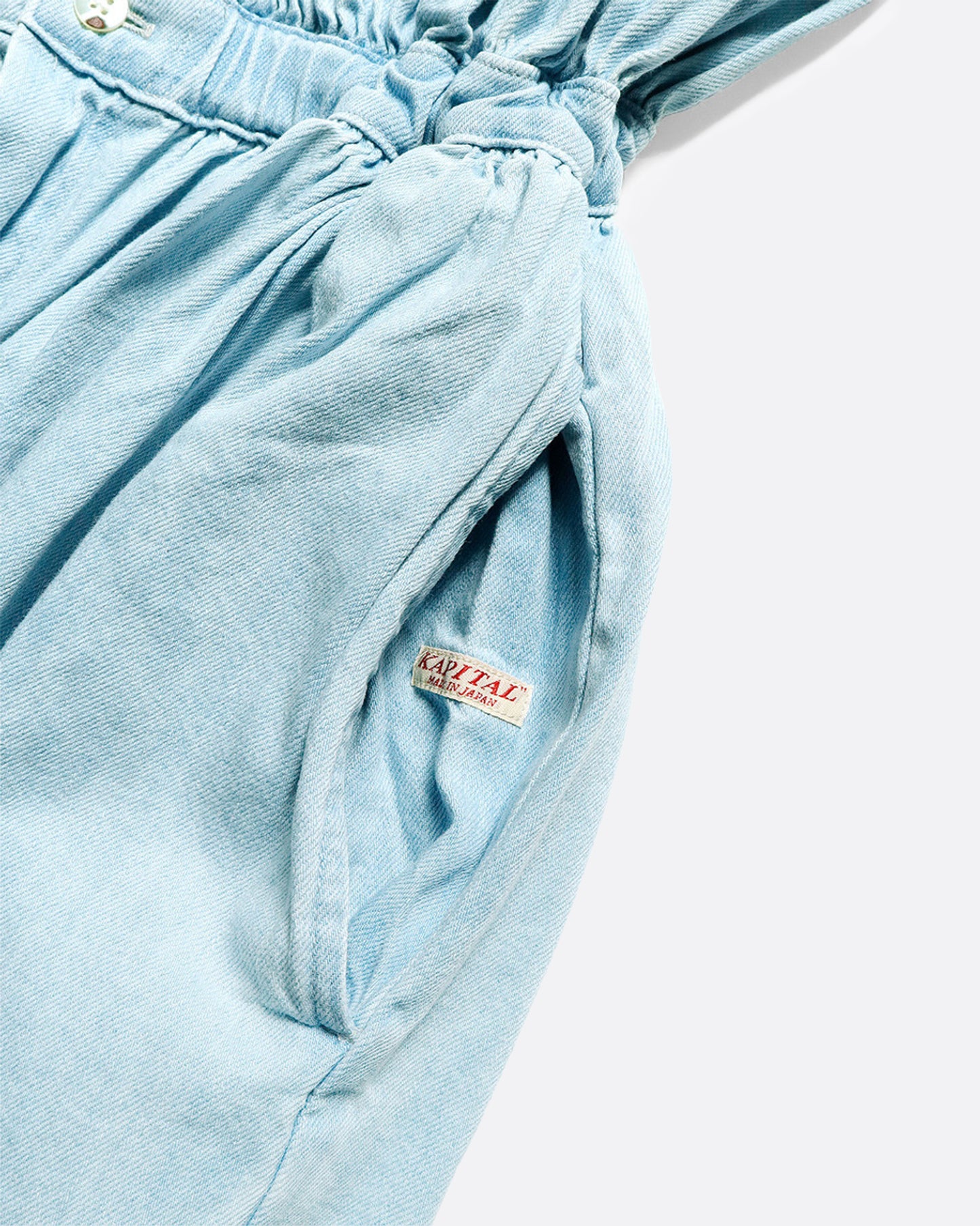 Sleeveless chambray jumpsuit with gathered waist, ruched bust and wide legs. Close up view of hidden pocket opening with concealed "Kapital" tag. 