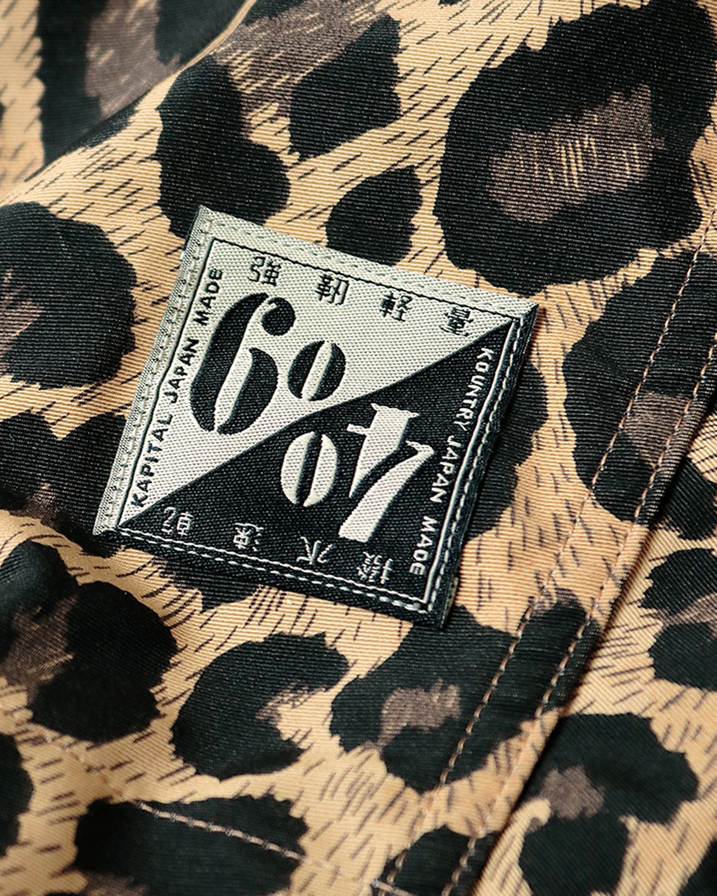 Cropped leopard rain jacket with hood and two front pockets. Close up view of branding.