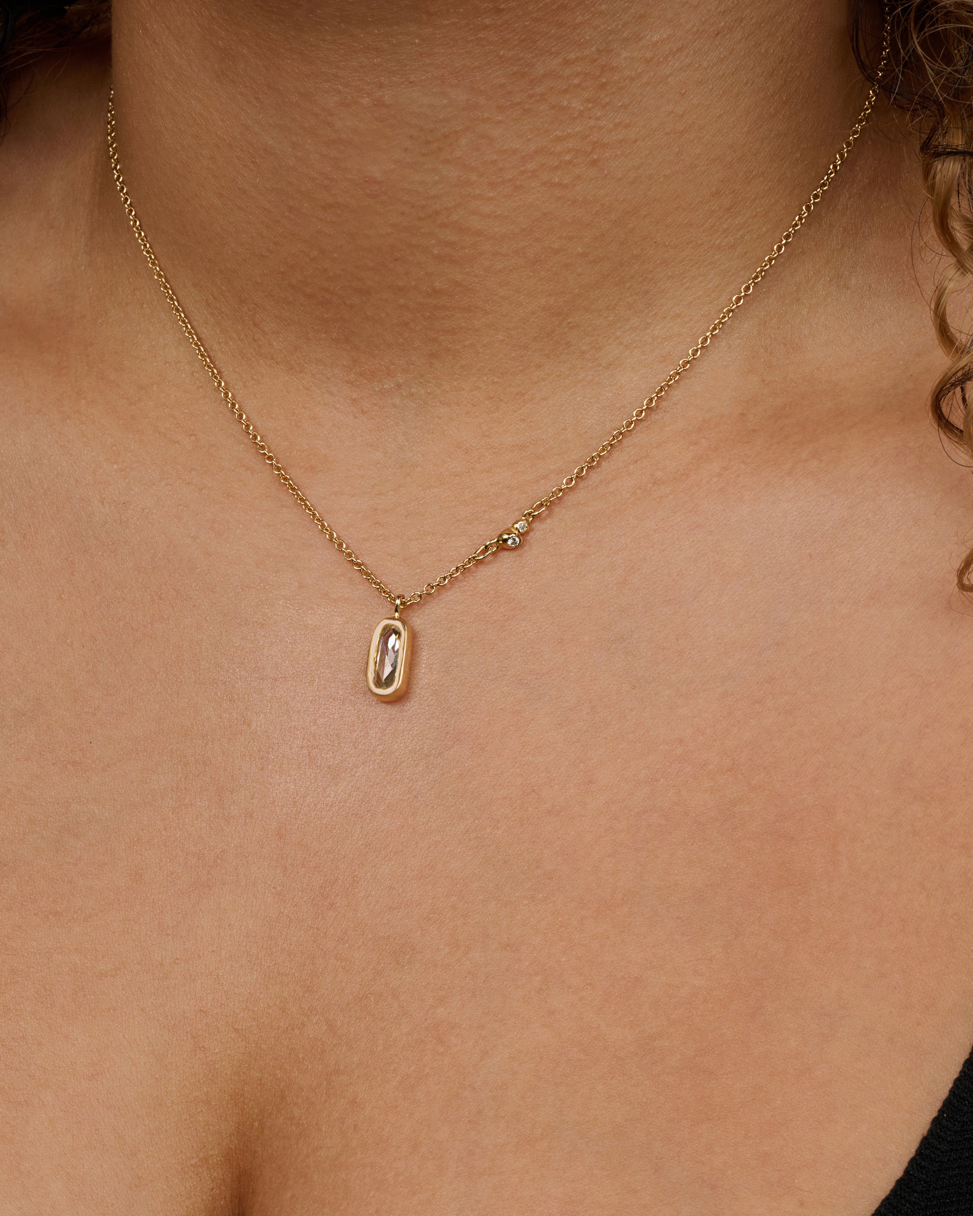 A yellow gold necklace with a rose cut solitaire diamond pendant and a cluster  of diamonds on the chain. View of the necklace worn.