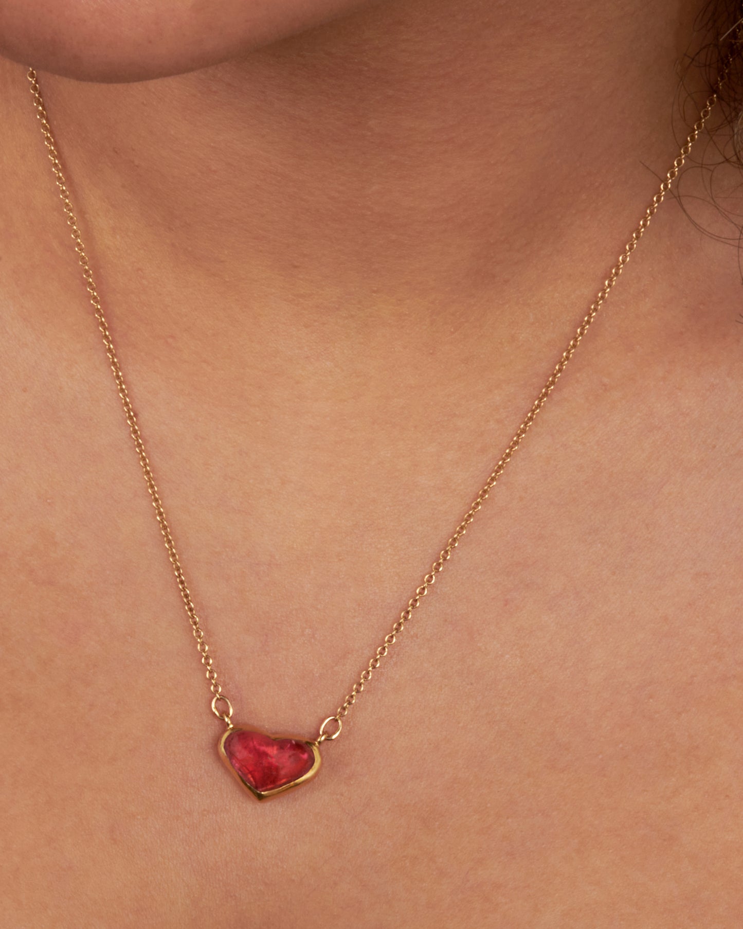 This 18k gold chain holds a unique watermelon rubellite heart encased in a gold bezel setting. View on a neck.