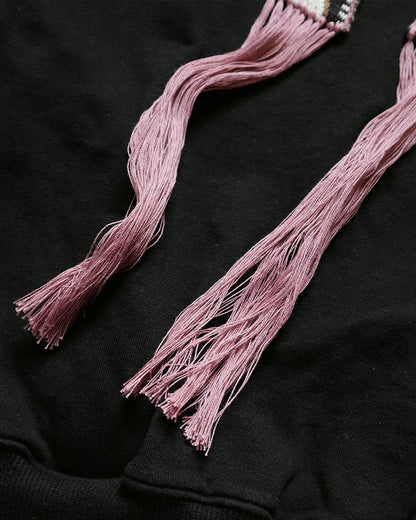 Black hooded sweatshirt with woven tassel drawstrings, close view of the pink tassels