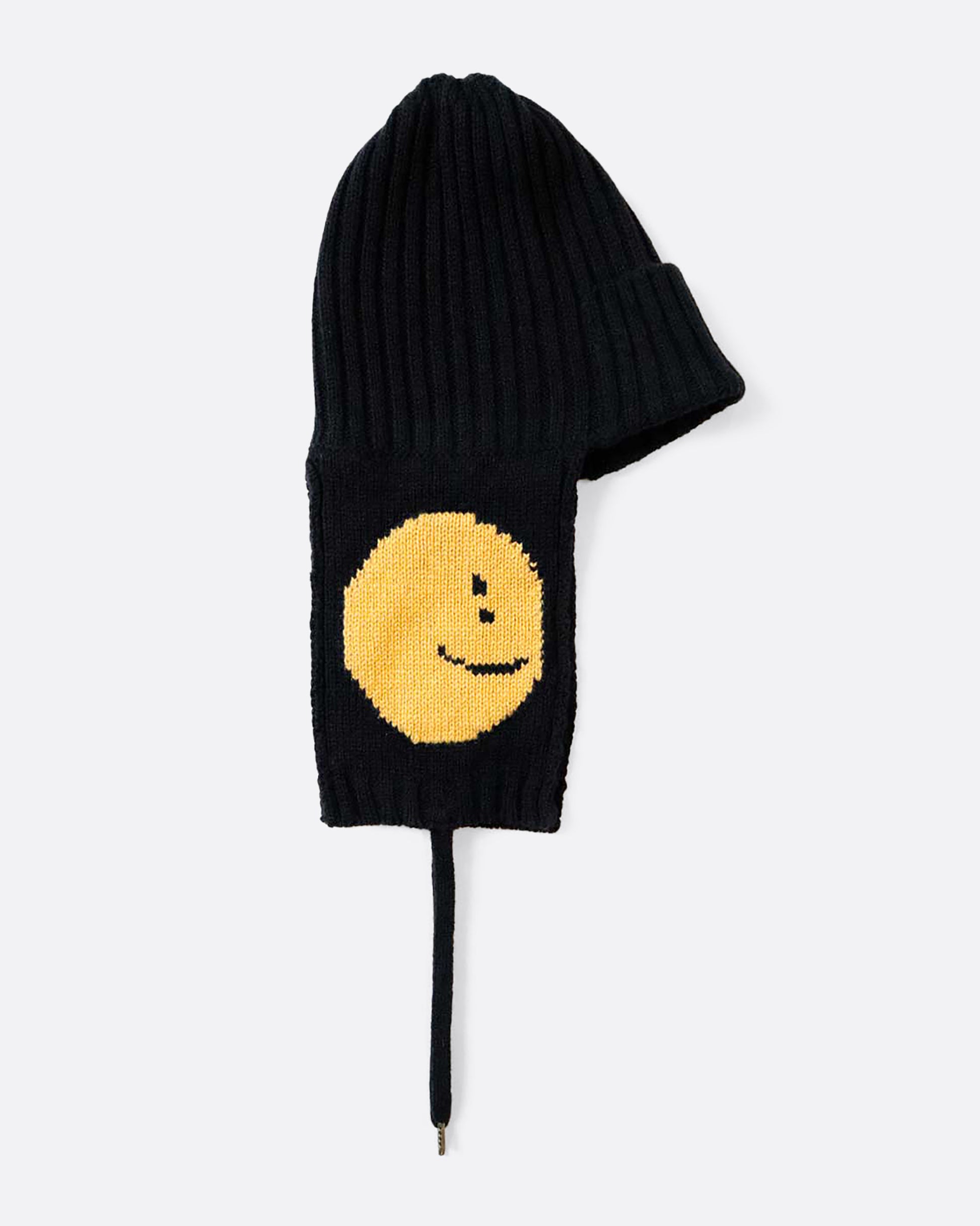 A black knit hat with yellow smilie faces on either ear flap. View from the alternate side, laying flat.